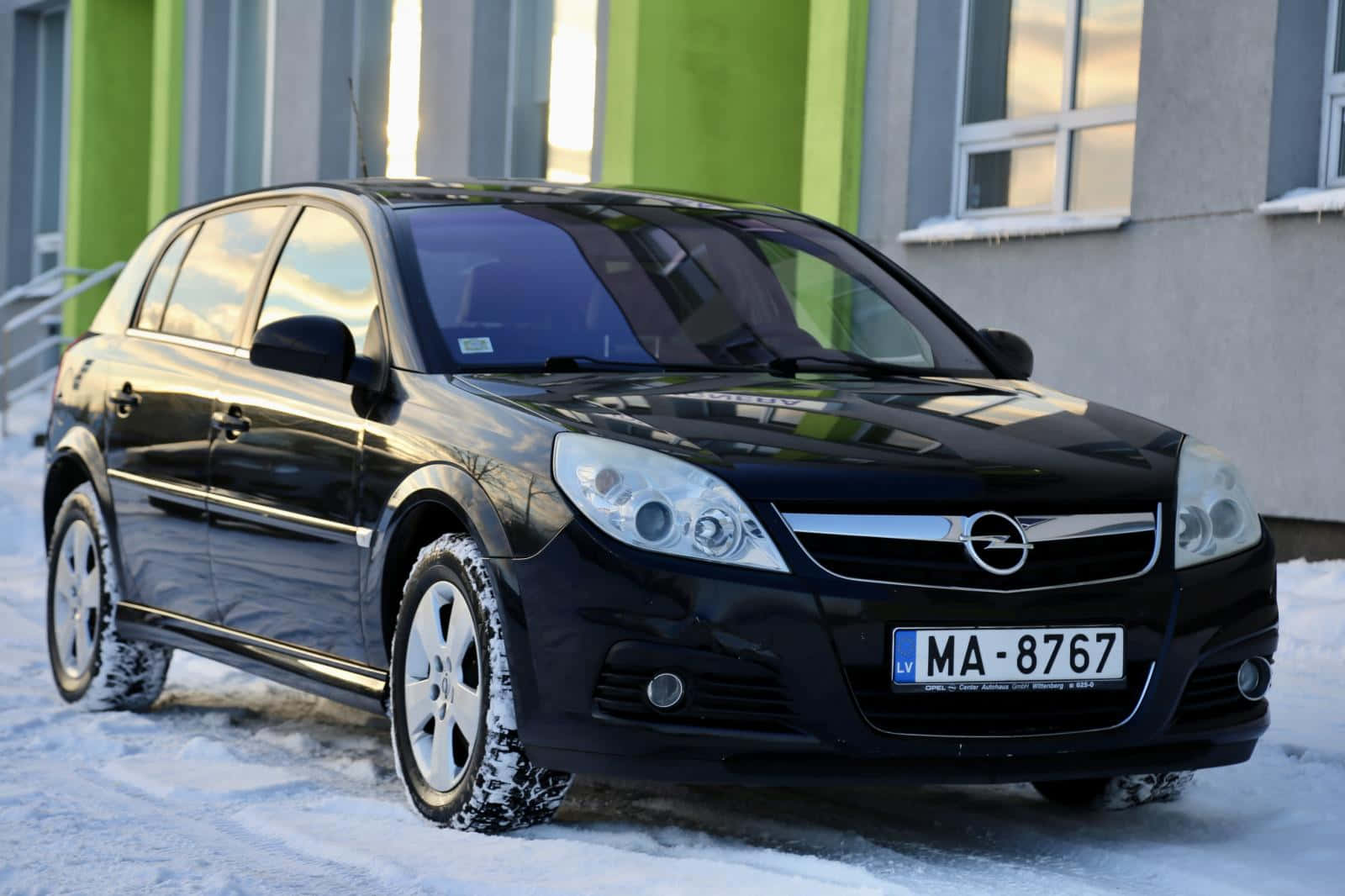  壁紙 — 一輛時尚的黑色Opel Astra停泊在雪地上，背景是一座現代建築。
