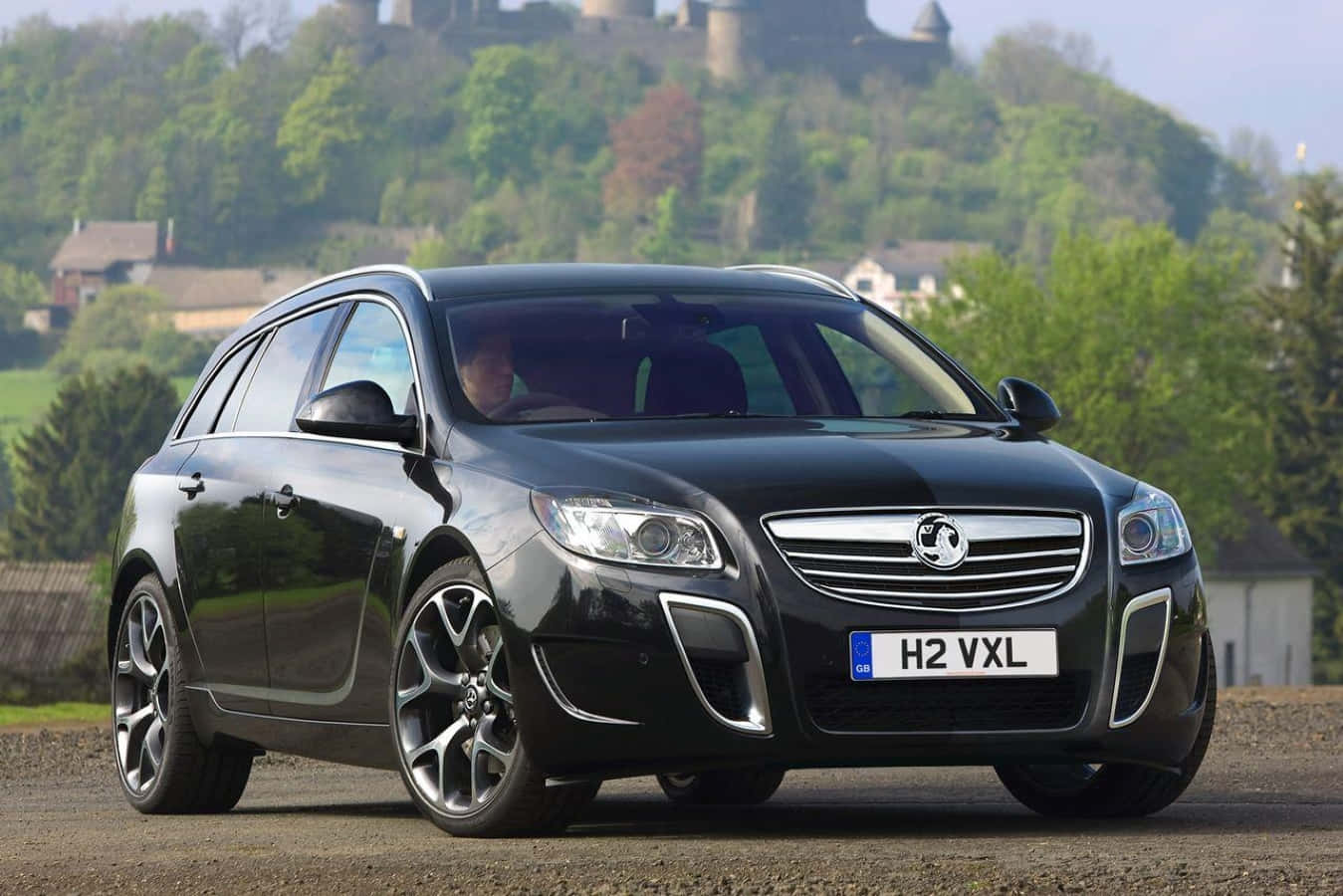 Opel Insignia 桌布 壁紙 — 一架時尚的黑色歐寶Insignia Sports Tourer停泊在碎石上，背景有城堡和綠色山丘。