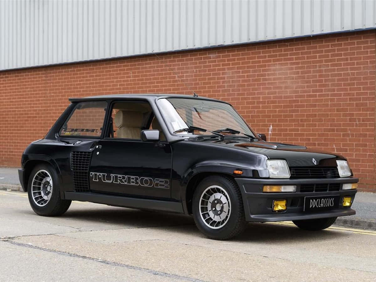 Renault 5 Turbo 桌布 壁紙 — 一輛時尚的黑色雷諾5 Turbo 2跑車停放在磚牆前，牆上有波紋金屬屋頂。