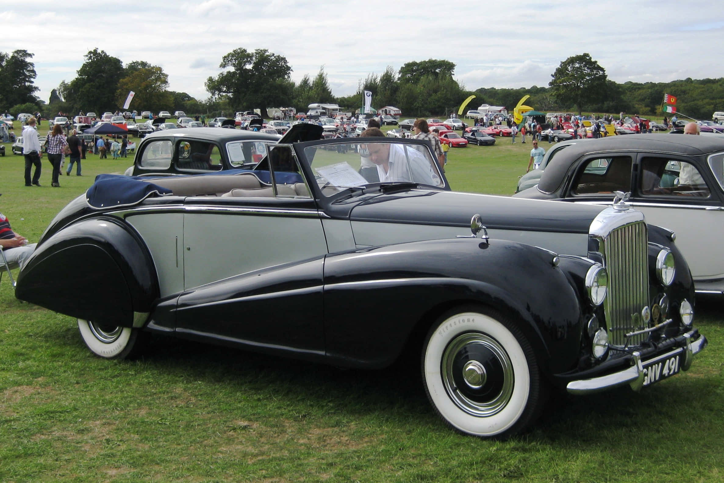 Bentley Mark Vi 桌布 壁紙 — 一輛時尚的黑色和銀色復古敞篷車，配備白色輪胎，在經典車展的草地上閃閃發光。