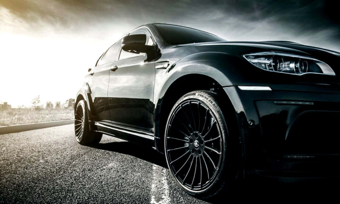 Bmw X6 桌布 壁紙 — 一輛配備定制輪轂的時尚黑色跑車，在空蕩的瀝青路上，於戲劇性的日落光線下閃閃發光。