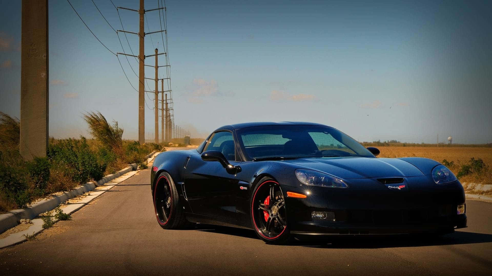 Chevrolet Corvette C5 桌布 壁紙 — 一輛時尚的黑色跑車，配備紅色輪圈，停在沙漠公路上，天空湛藍清澈。