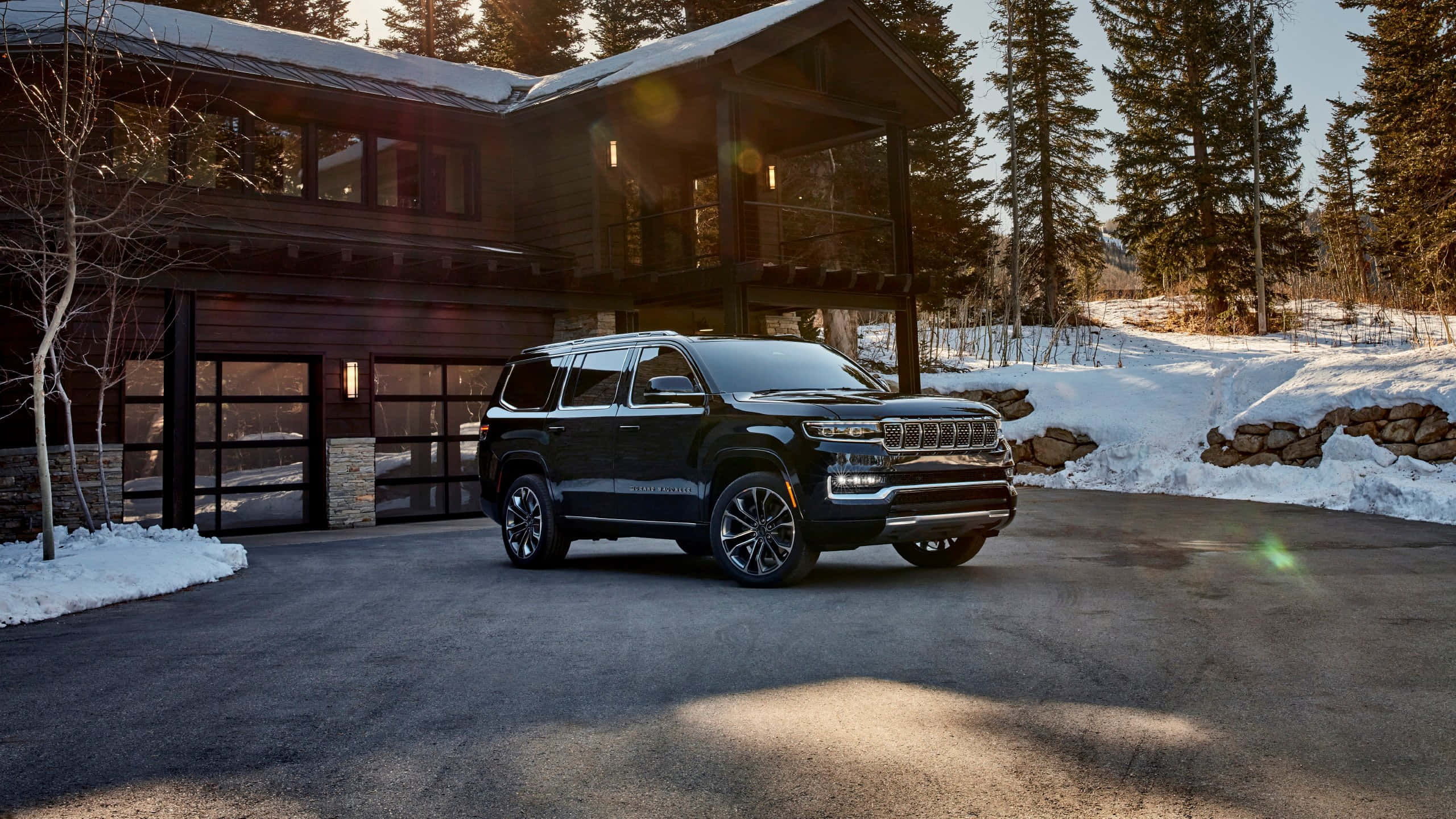 Jeep Wagoneer 桌布 壁紙 — 一輛時尚的黑色SUV停在現代木屋前，周圍是黃金時段被雪覆蓋的松樹。