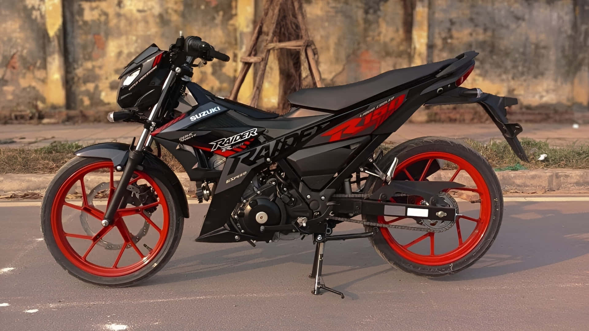  壁紙 — 一架型格黑色鈴木 Raider 125 電單車，配以鮮紅色車輪，停泊在陽光明媚的街道上，背景是風化了的牆壁。