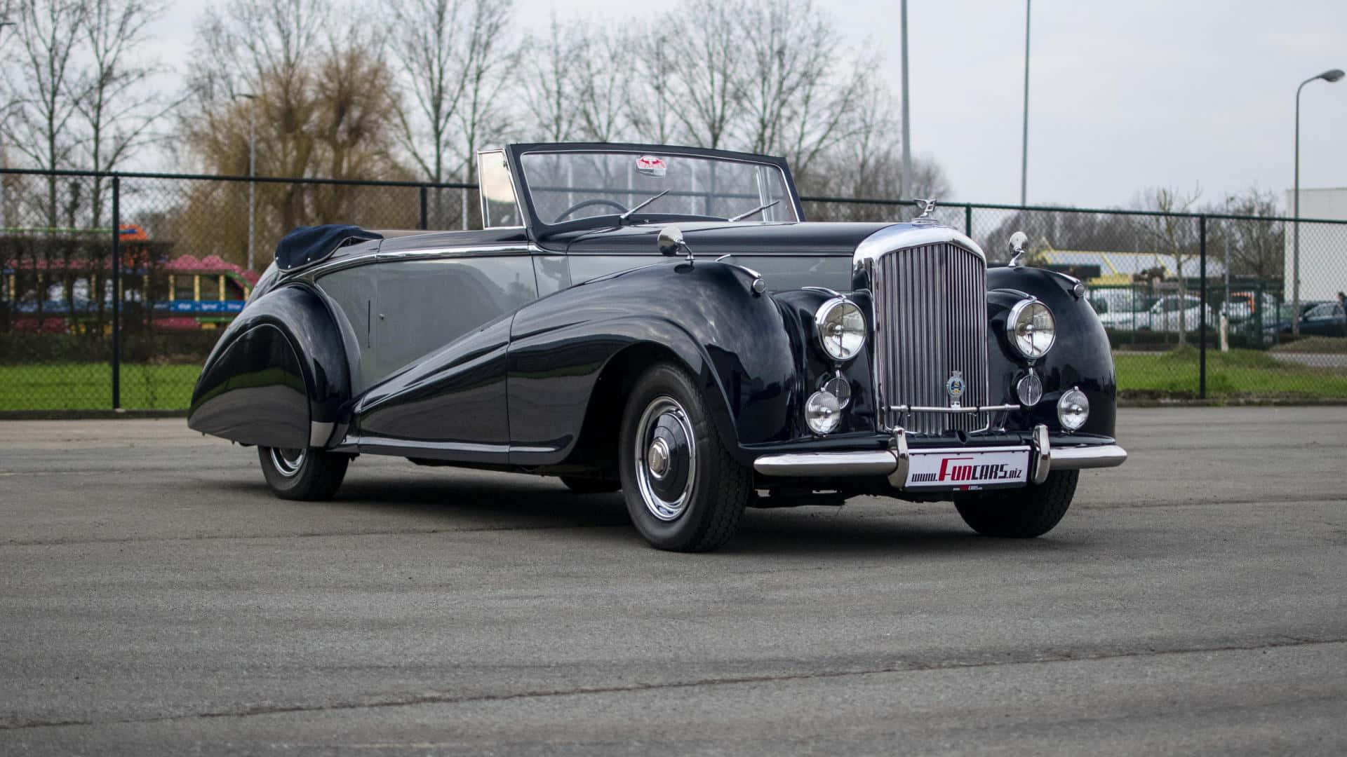 Bentley Mark Vi 桌布 壁紙 — 一輛時尚的黑色復古敞篷車，帶有鍍鉻裝飾，停在陰天下的瀝青路面上。