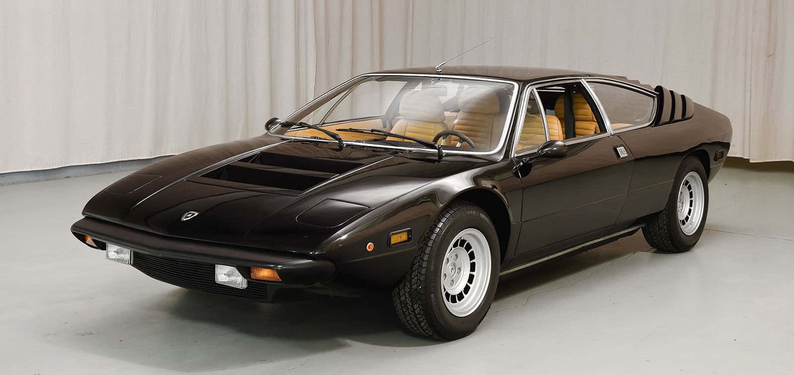 Lamborghini Urraco 桌布 壁紙 — 一輛時尚的黑色復古跑車，配以米色內飾，在簡約的攝影棚環境中展示。