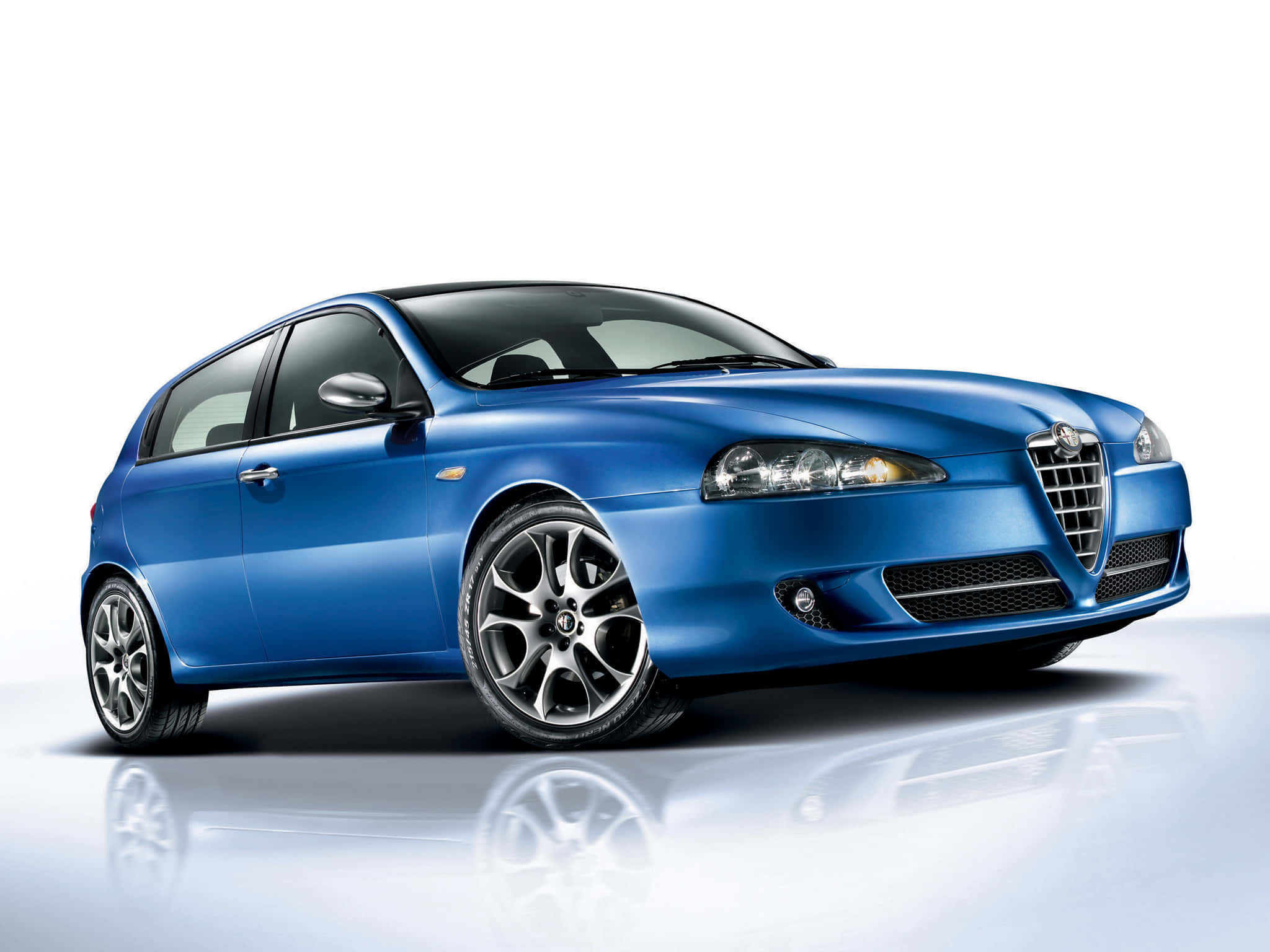 Alfa Romeo 147 桌布 壁紙 — 一輛時尚的藍色愛快羅密歐掀背車在攝影棚燈光下閃耀，白色地板上映出光澤倒影。
