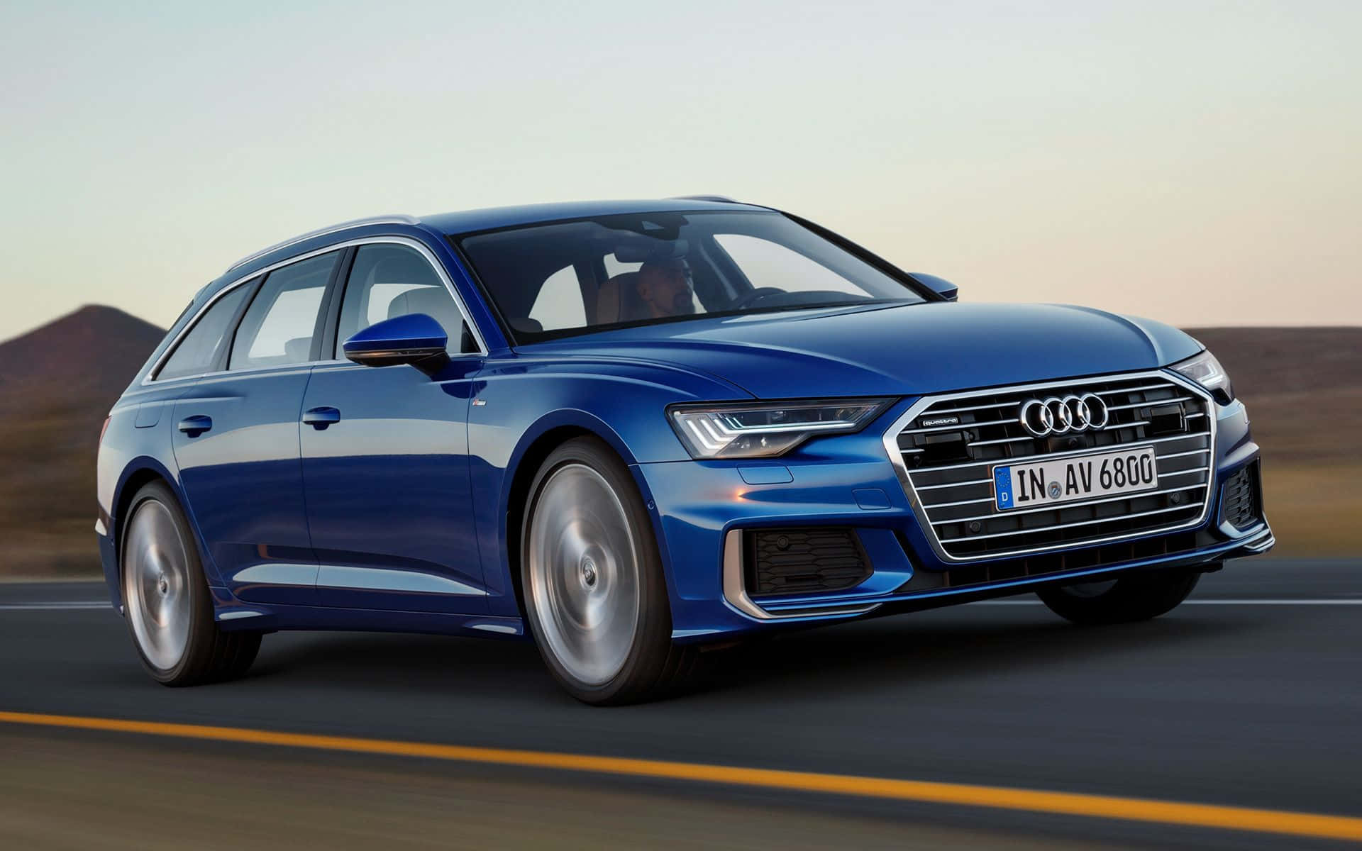 Audi A6 桌布 壁紙 — 一輛時尚的藍色奧迪旅行車在日落時分沿著沙漠高速公路疾馳，帶有模糊的動態和溫暖的環境光。
