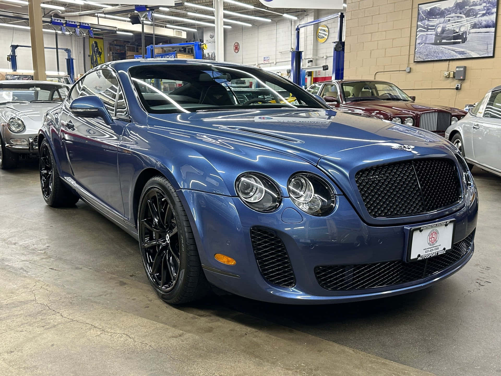Bentley Continental Supersports 桌布 壁紙 — 一輛時尚的藍色賓利 Continental GT 在明亮的車庫燈光下閃閃發光，周圍環繞著經典汽車。