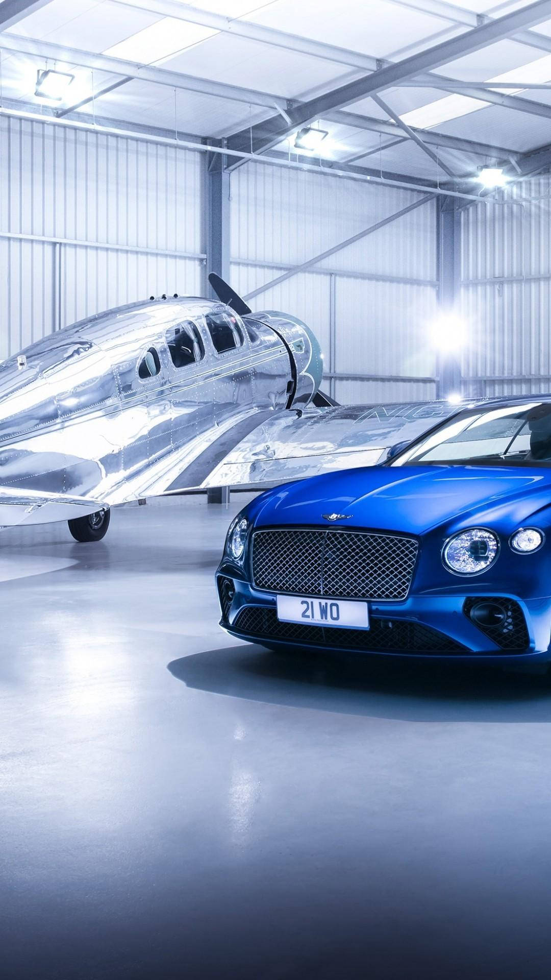 藍色 Bentley 汽車和銀色飛機在拋光機庫中。