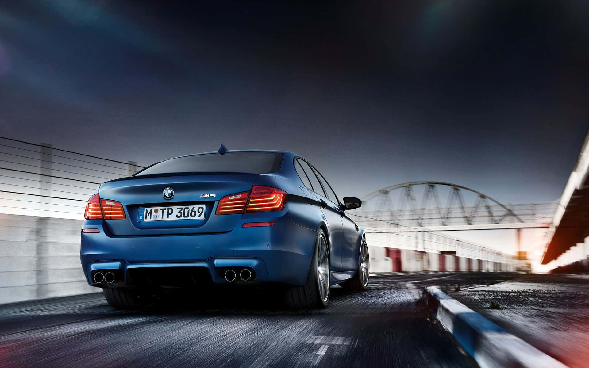Bmw M5 桌布 壁紙 — 一輛時尚的藍色BMW M5在黃昏時分沿著賽道飛馳，帶有動態模糊和發光的尾燈。