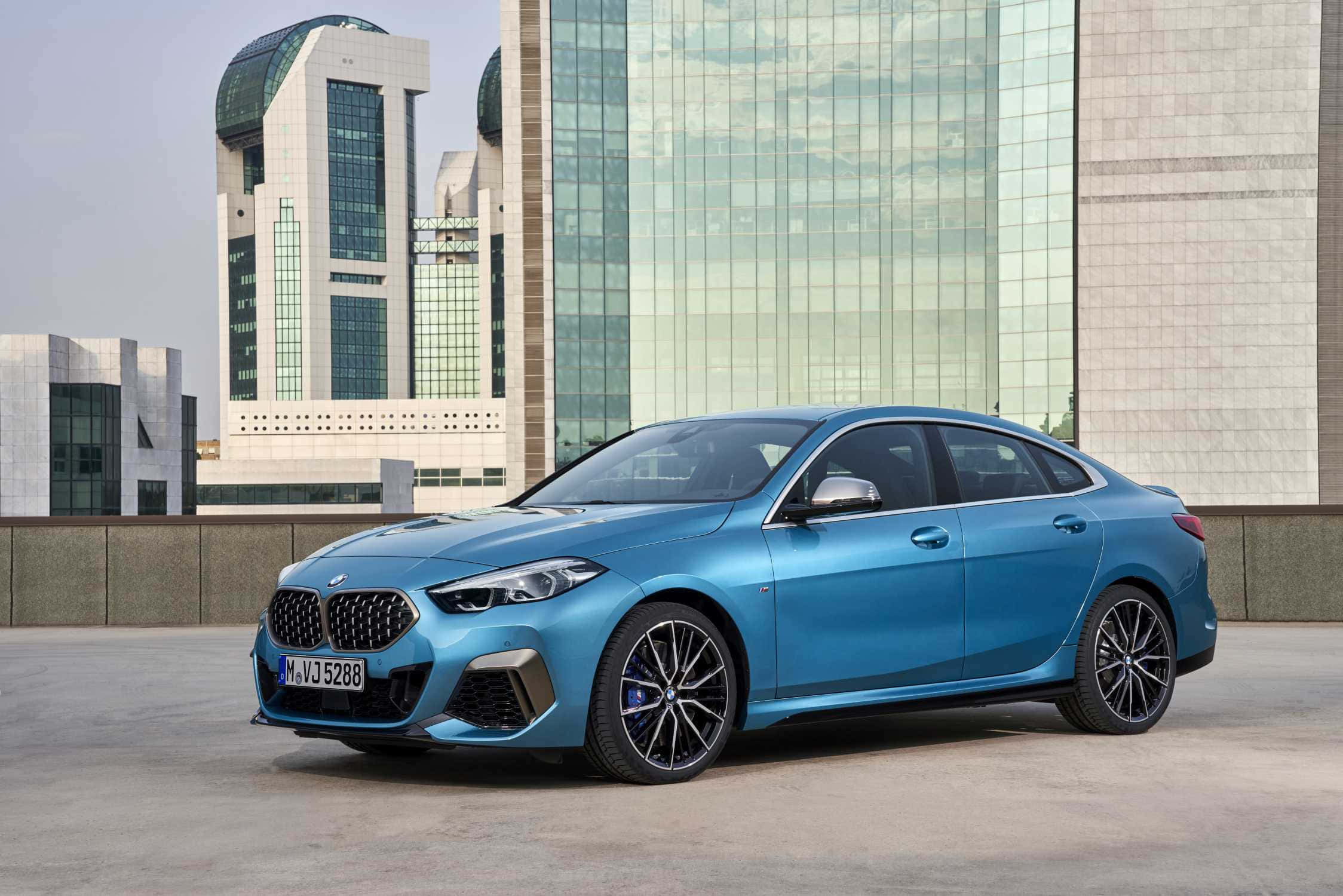 Bmw 2 Series 桌布 壁紙 — 一架時尚的藍色寶馬房車停泊在天台上，現代玻璃摩天大樓在其閃亮表面反射。