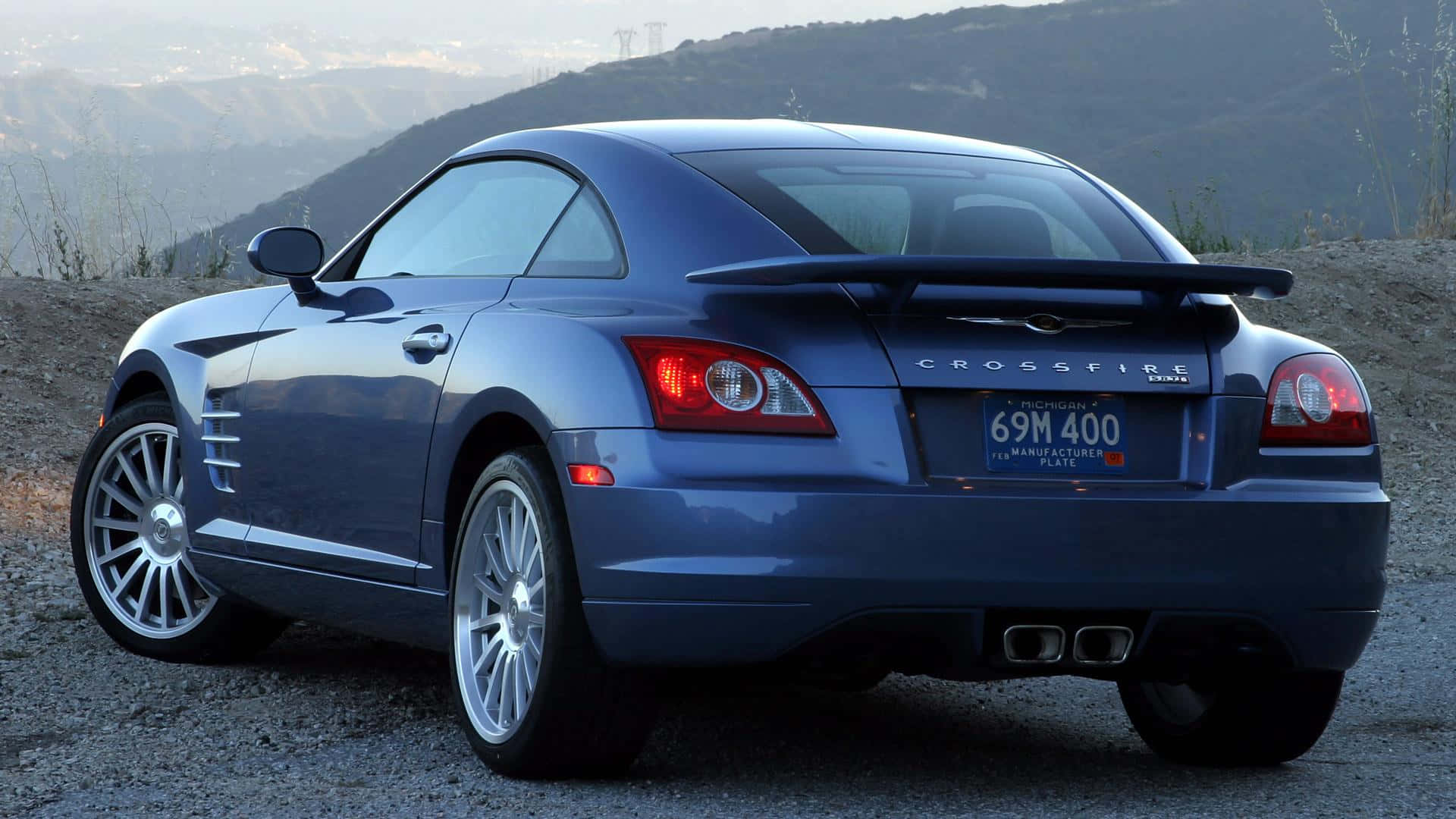 Chrysler Crossfire 桌布 壁紙 — 一架流線型藍色 Chrysler Crossfire 跑車停泊在碎石山坡上，背景有山巒。