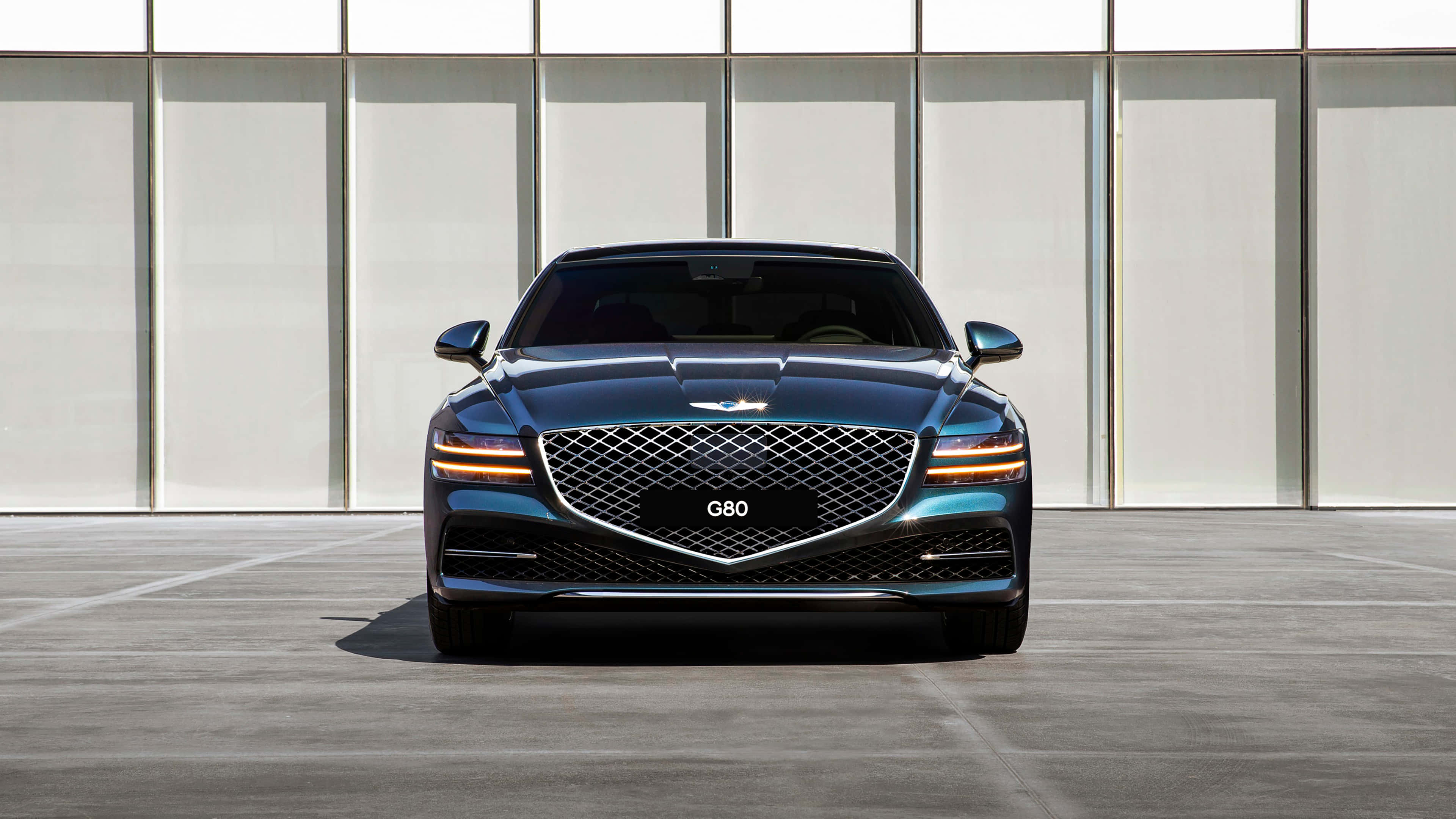 Genesis G80 桌布 壁紙 — 一輛時尚的藍色Genesis G80豪華轎車正面朝前，配備發光頭燈，背景是簡約現代建築外牆。