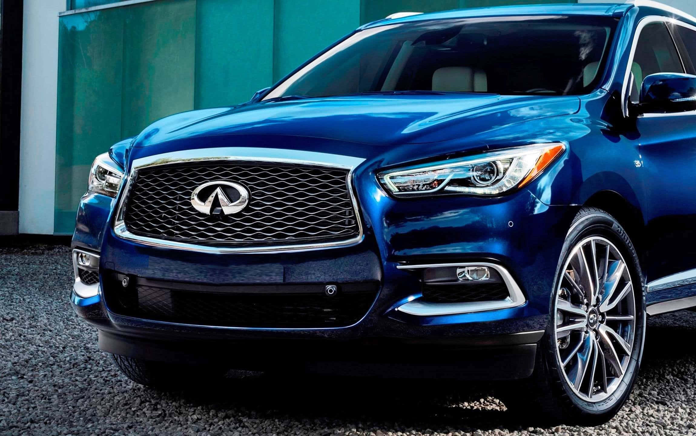 Infiniti Qx60 桌布 壁紙 — 一輛時尚的藍色 Infiniti SUV 在明亮光線下閃耀，帶有鍍鉻飾條和現代車頭燈，停在礫石上，靠近一座青綠色建築。