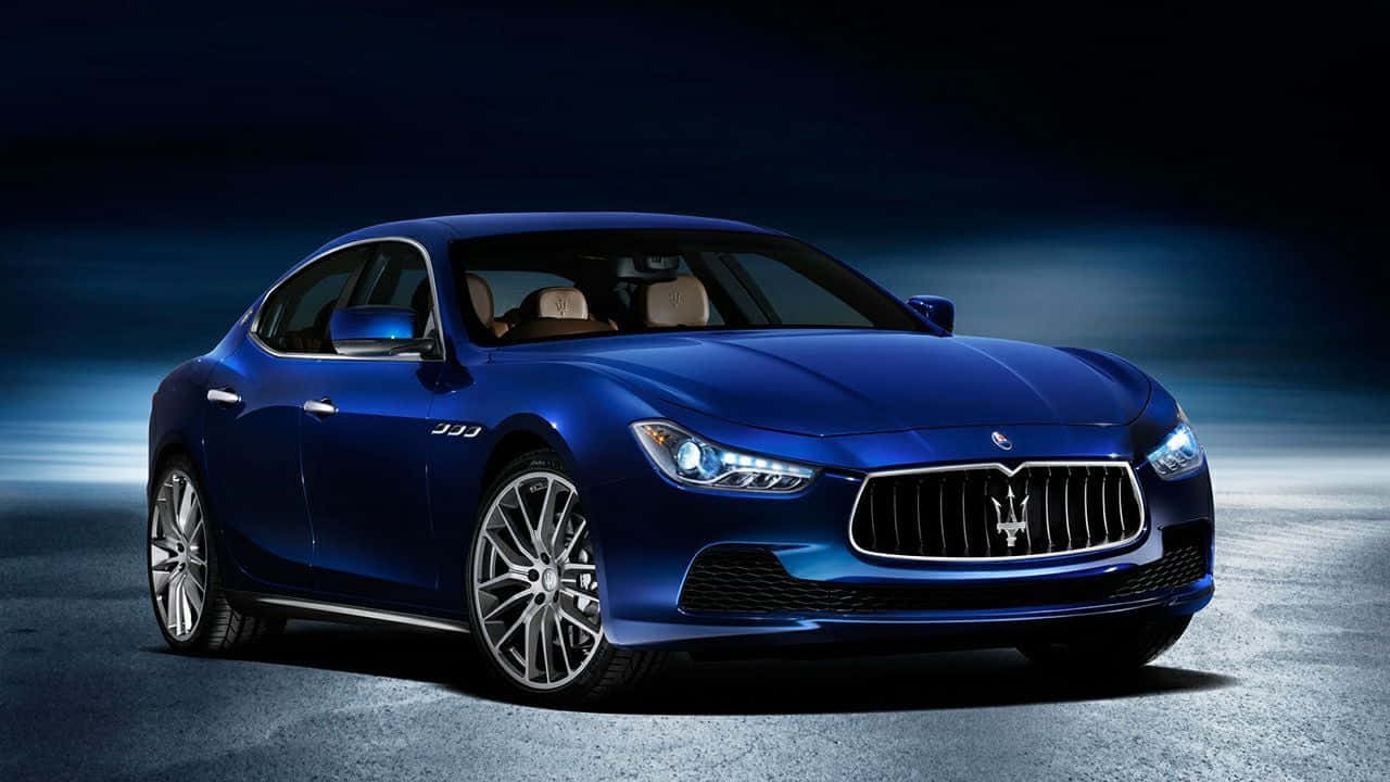 Maserati Ghibli 桌布 壁紙 — 一輛時尚的藍色瑪莎拉蒂跑車在戲劇性的攝影棚燈光下，在深色瀝青路面上閃閃發光。