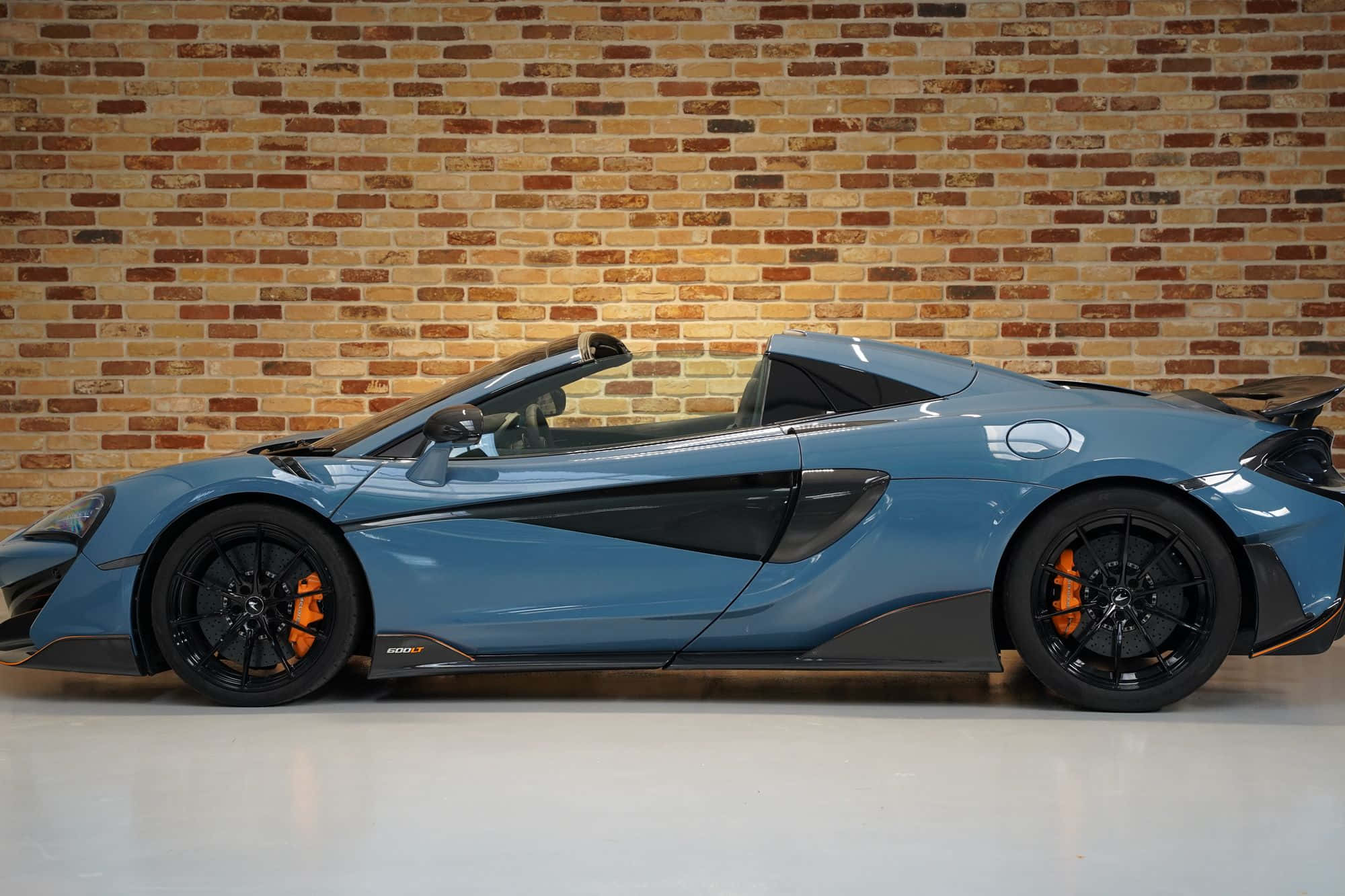 Mclaren 600lt Spider 桌布 壁紙 — 一輛時尚的藍色McLaren Speedtail開篷跑車，帶有橙色制動卡鉗，側面靠在溫暖的磚牆上。