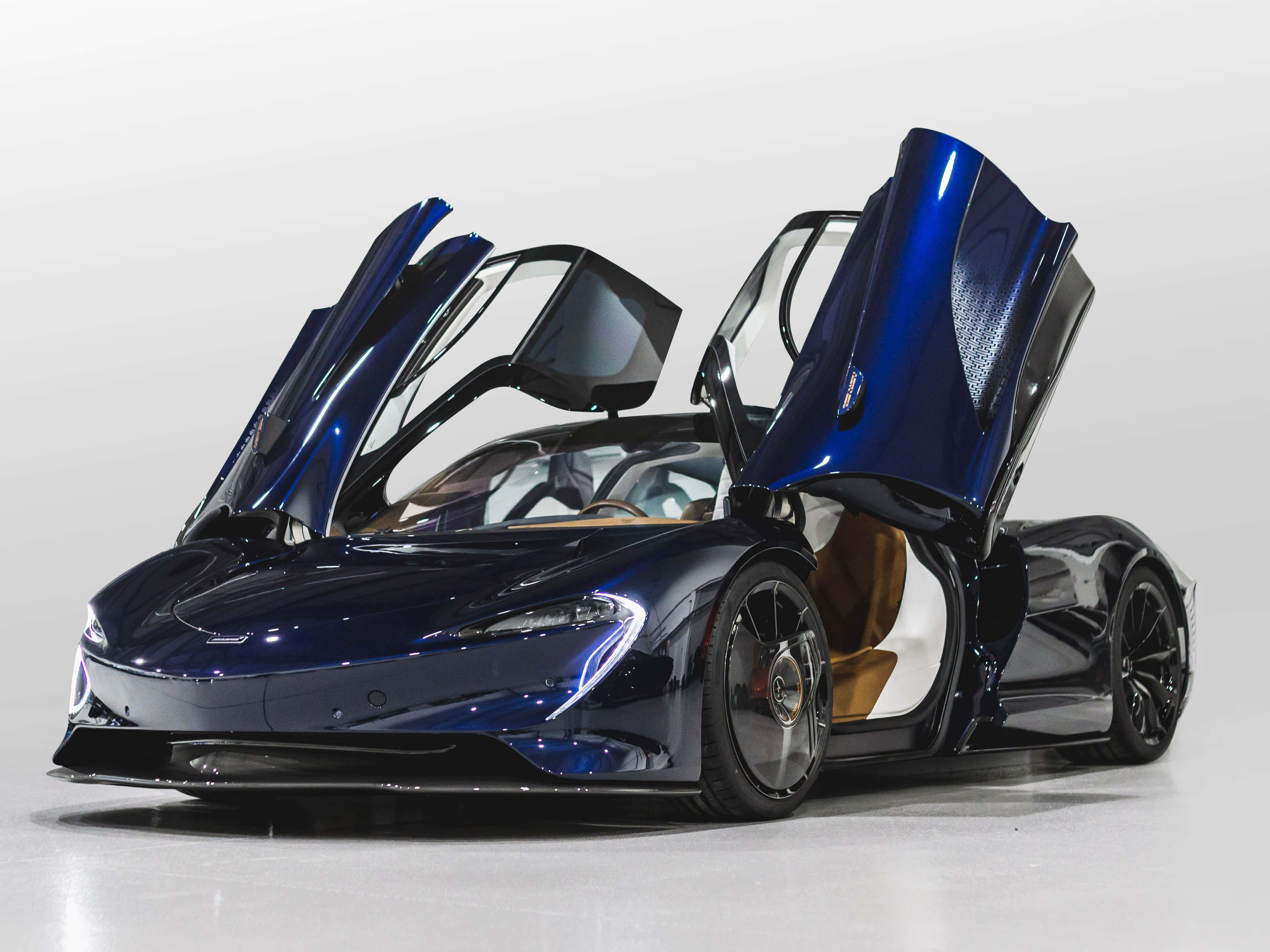 Mclaren Speedtail 桌布 壁紙 — 一架流線型藍色McLaren超級跑車，鷗翼門打開，背景是簡約的白色工作室。
