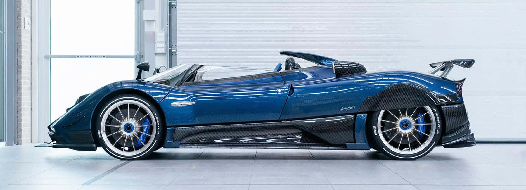 Pagani Zonda Hp Barchetta 桌布 壁紙 — 一輛時尚的藍色Pagani Huayra敞篷跑車在潔白車庫的明亮燈光下閃閃發光。