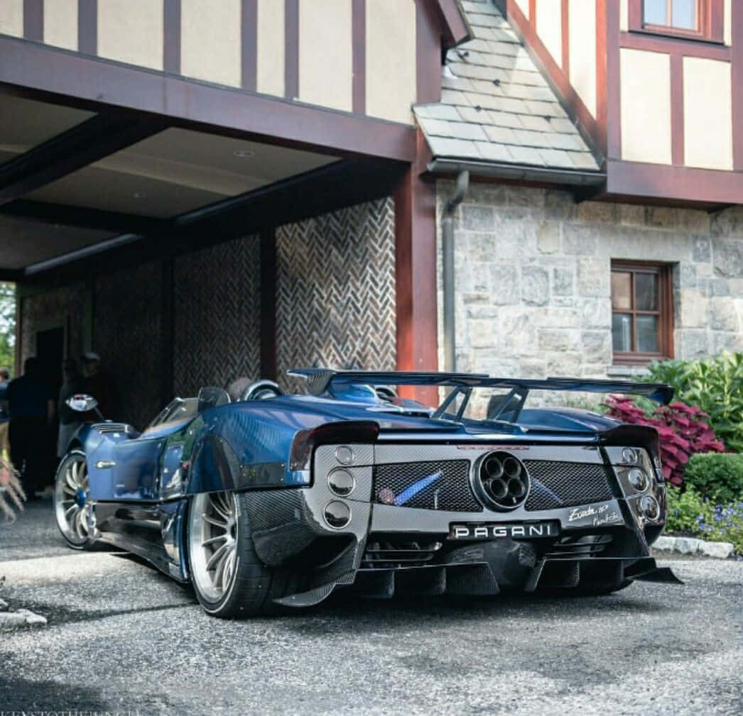 Pagani Zonda Hp Barchetta 桌布 壁紙 — 一輛時尚的藍色Pagani Zonda R超級跑車停在質樸的石木建築前，附近有人。