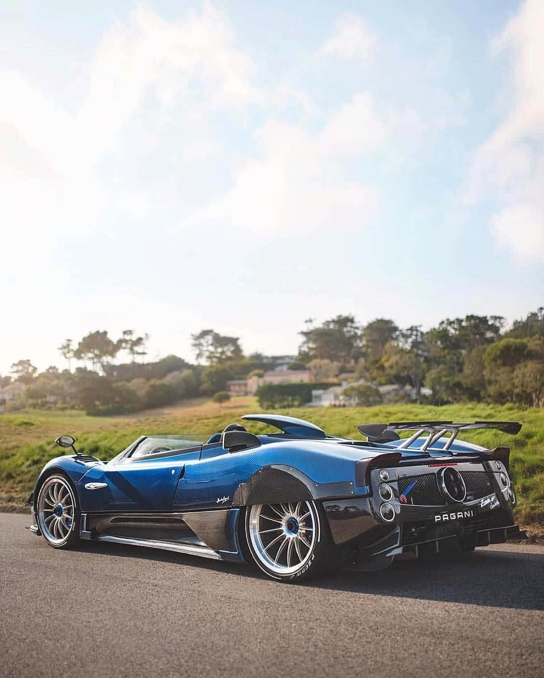 Pagani Zonda Hp Barchetta 桌布 壁紙 — 一輛時尚的藍色Pagani Zonda跑車停泊在陽光明媚的道路上，背景是綠色的山丘和樹木。