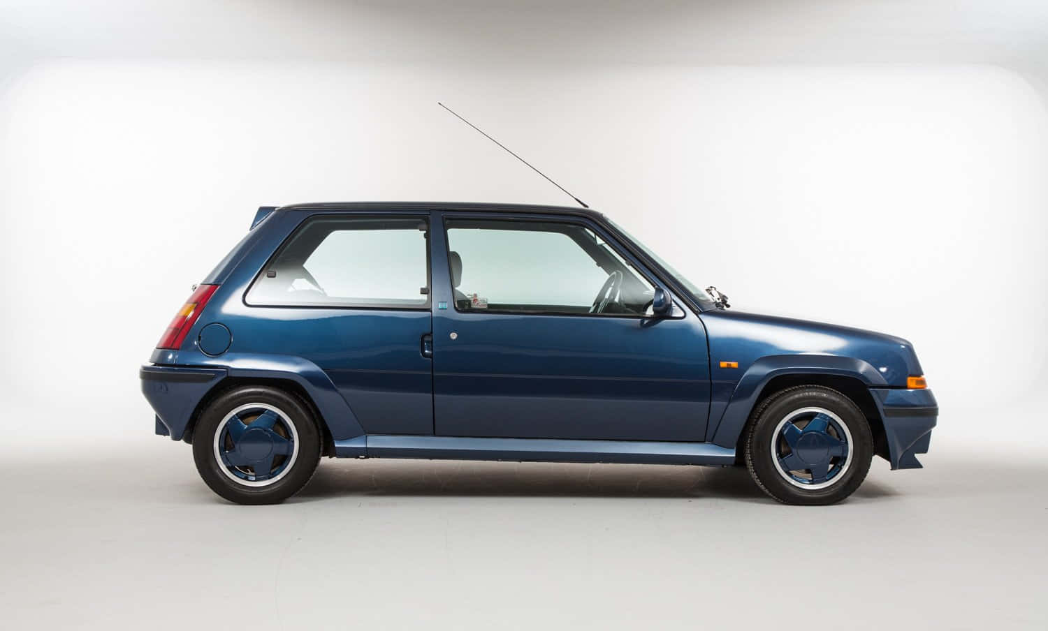 Renault 5 Turbo 桌布 壁紙 — 一部流線型藍色雷諾5 Turbo 2跑車，以側面輪廓展示在純白工作室背景前。