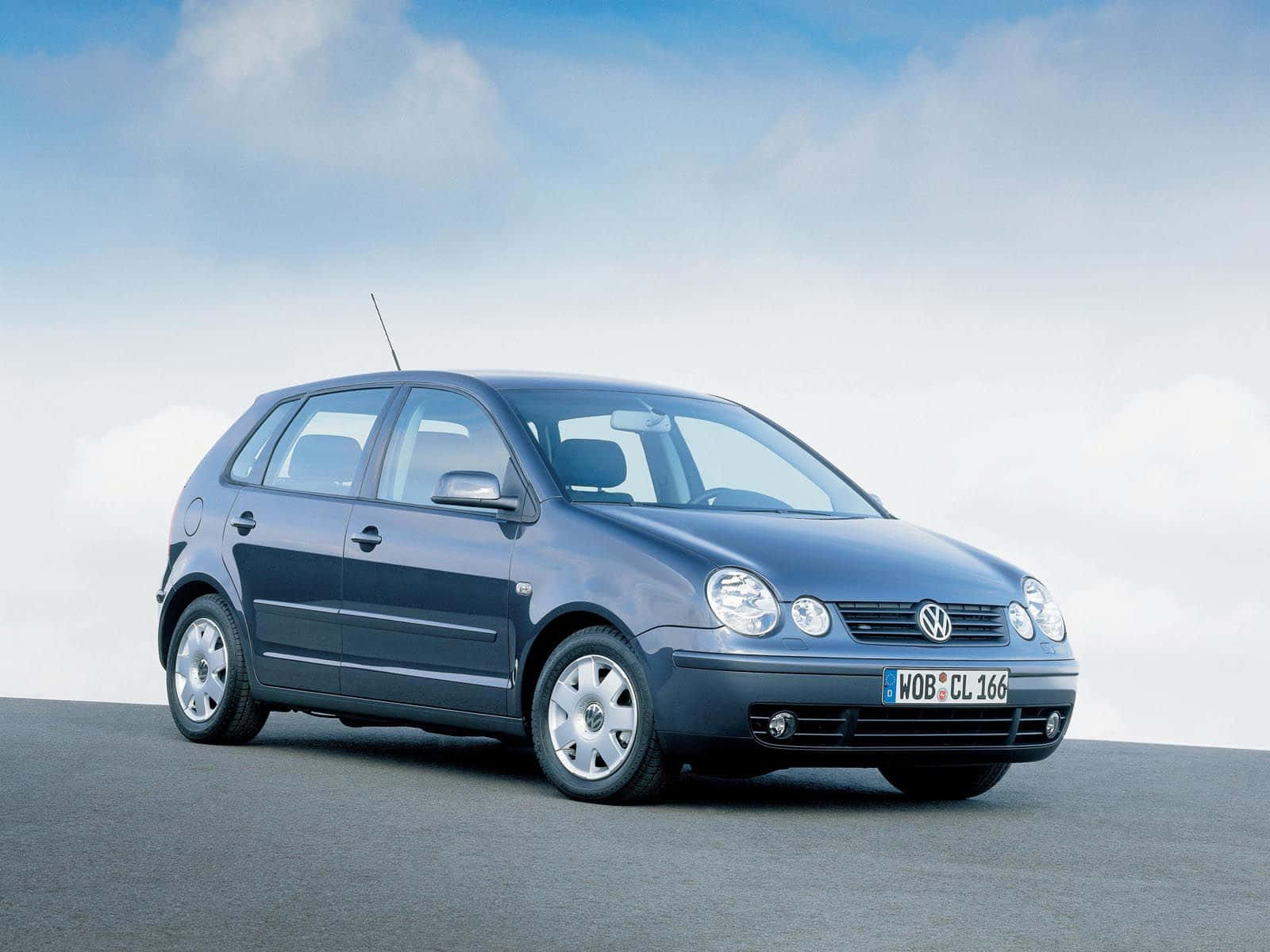 Volkswagen Polo 桌布 壁紙 — 一架時尚的藍色福士Polo掀背車停泊在灰色地面上，天空柔和藍色，帶有縷縷白雲。