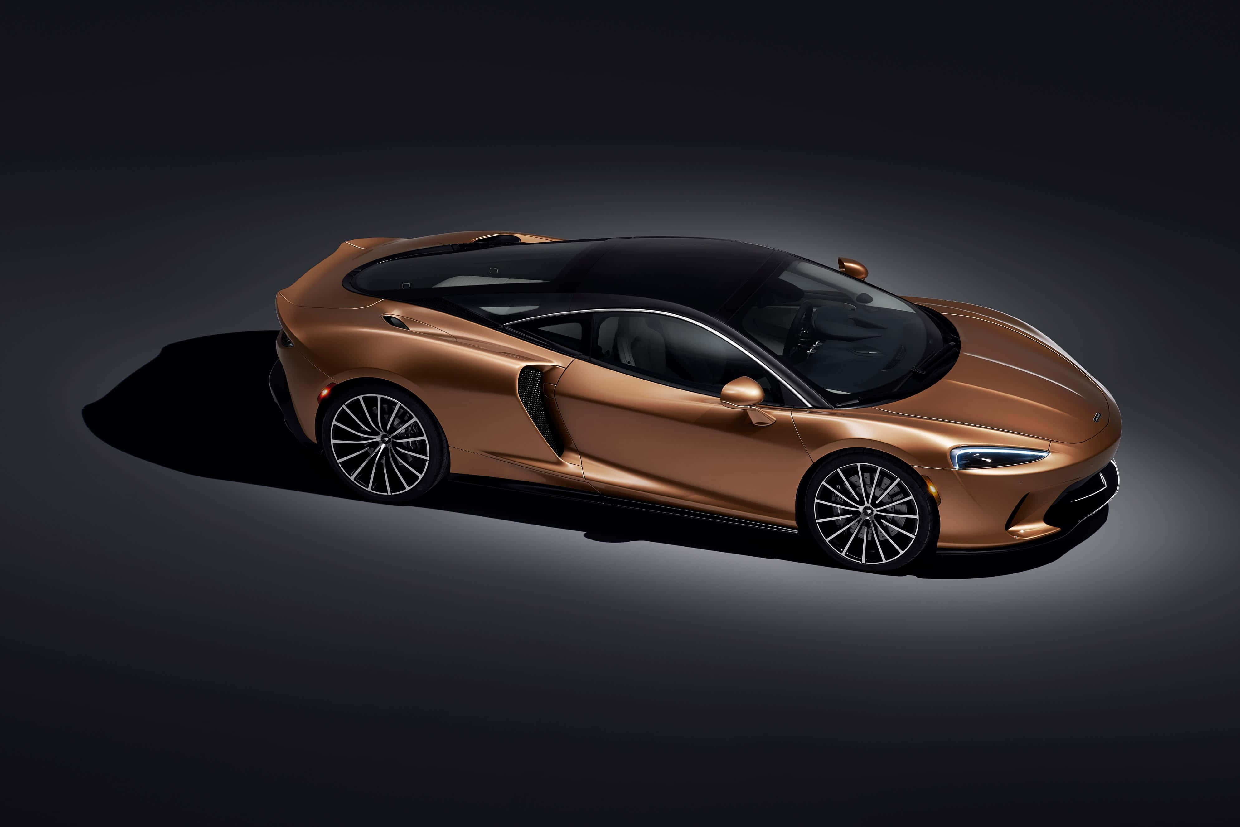 Mclaren Gt 桌布 壁紙 — 一輛帶黑色飾邊的時尚青銅色跑車，在戲劇性聚光燈下，於黑暗的攝影棚背景中滑行。