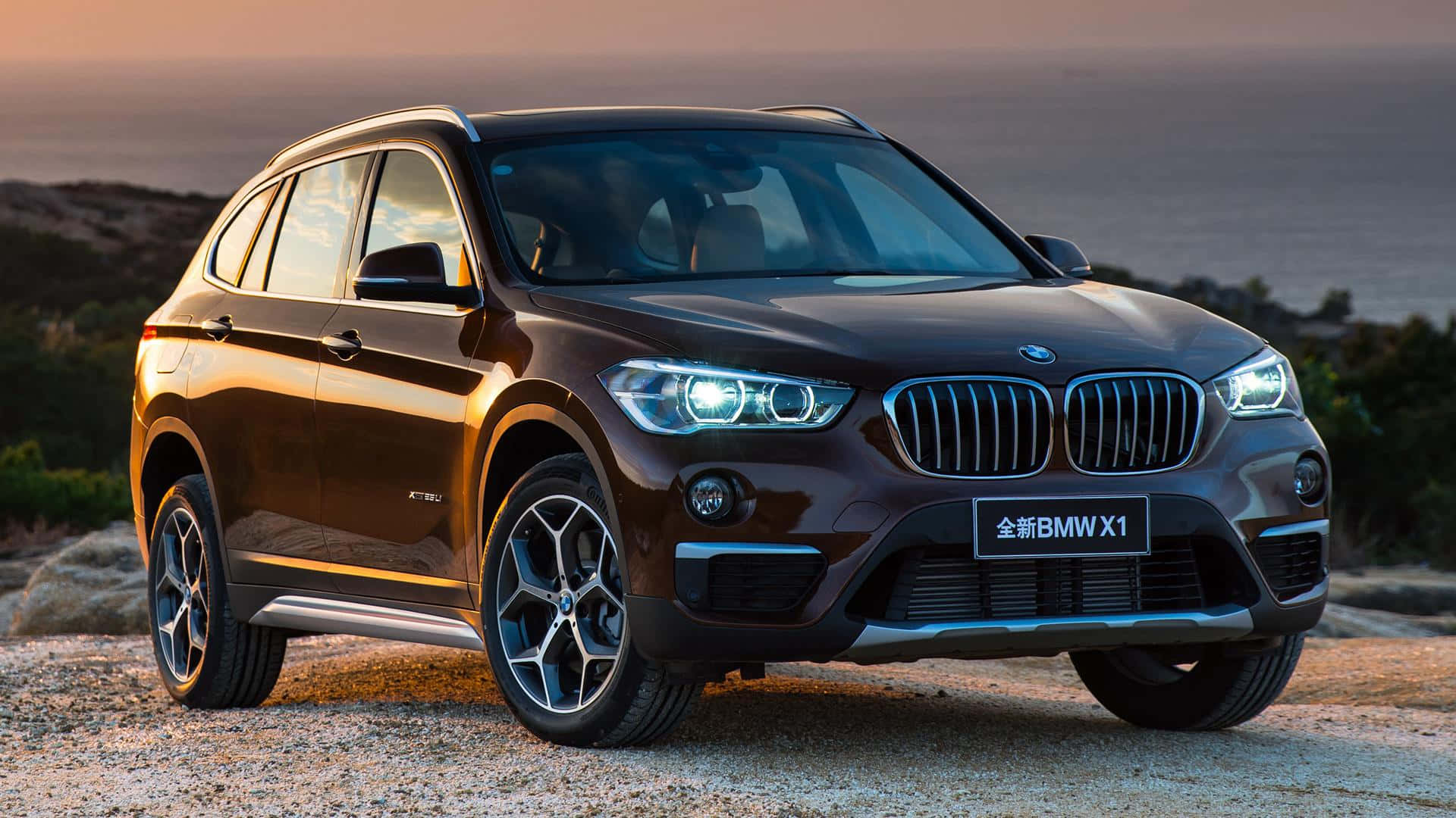 Bmw I8 桌布 壁紙 — 一輛時尚的棕色BMW X1 SUV在金色日落光芒下閃耀，停泊在俯瞰海洋的岩石海岸懸崖上。