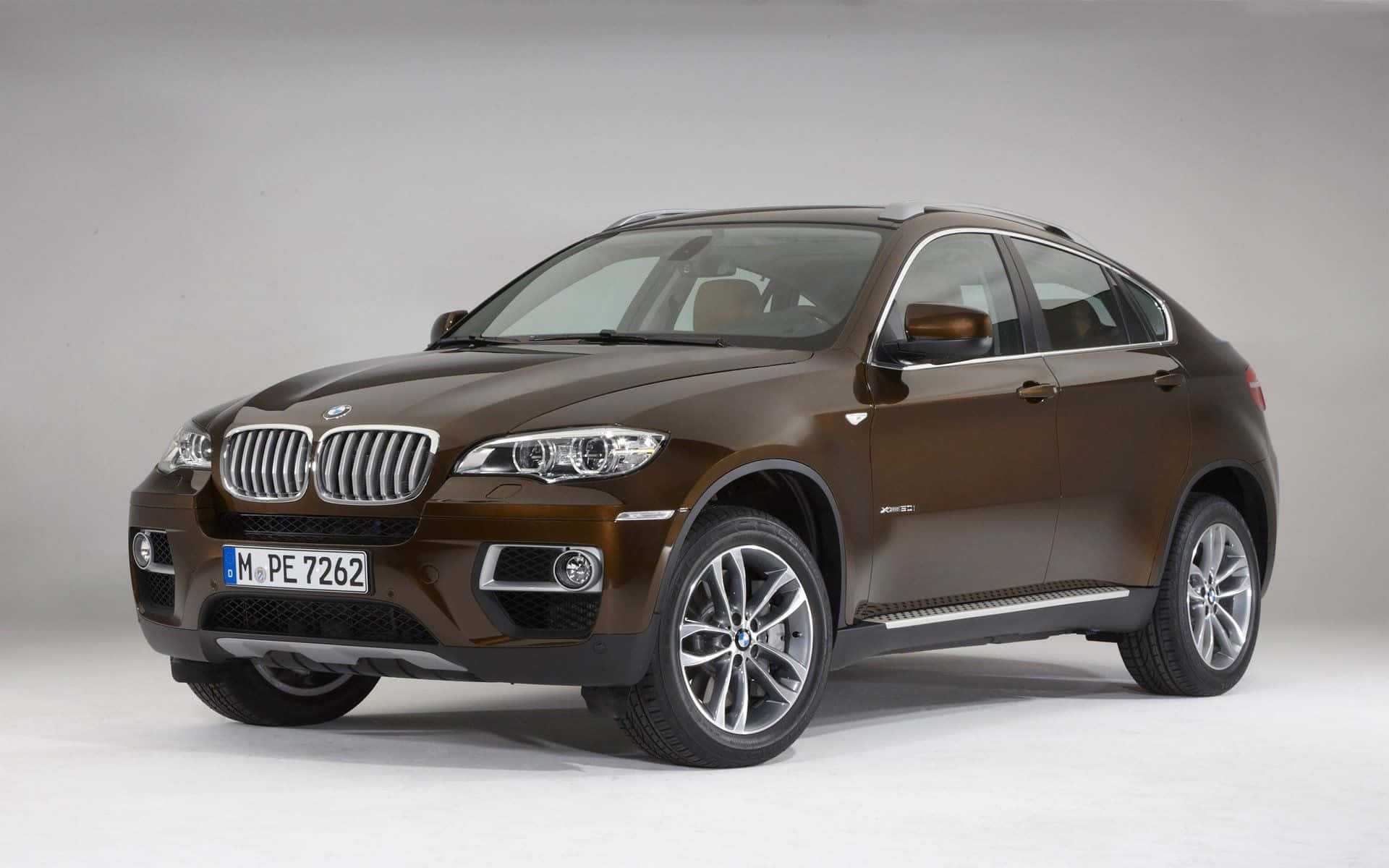 Bmw X6 桌布 壁紙 — 一輛時尚的棕色BMW X6 SUV，配備銀色輪圈和鍍鉻裝飾，在簡約的攝影棚背景前展現姿態。