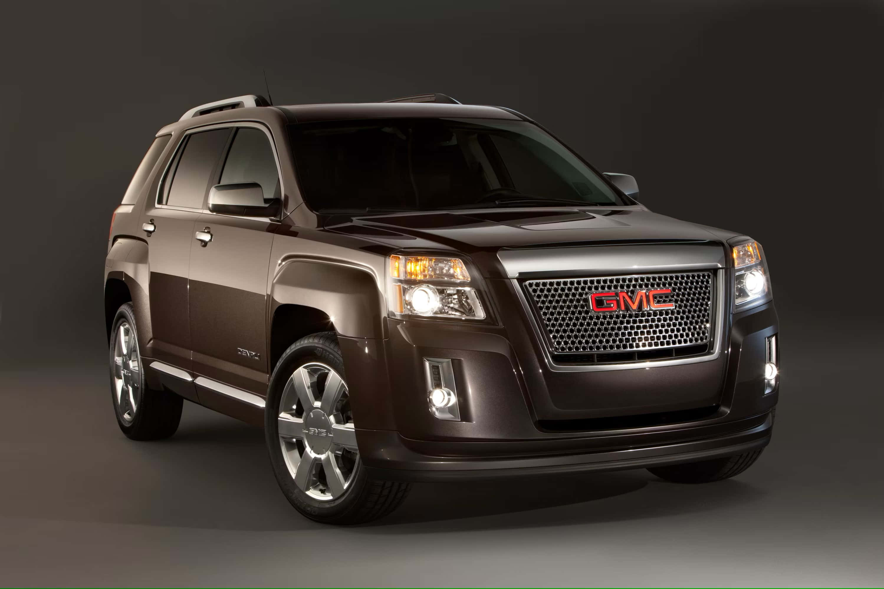 Gmc Terrain 桌布 壁紙 — 一輛時尚的棕色GMC Acadia SUV，帶有鍍鉻飾邊和發光頭燈，在深色工作室背景下展示。