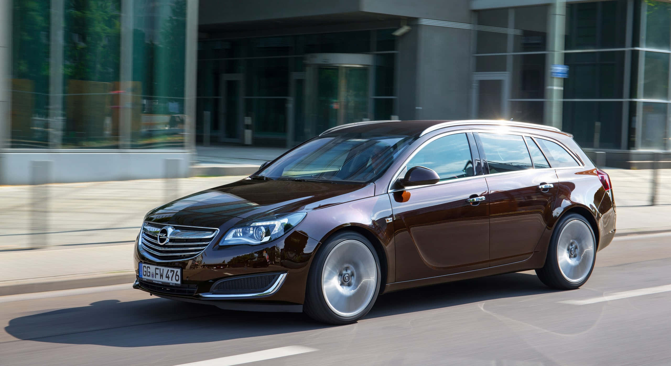 Opel Insignia 桌布 壁紙 — 一輛時尚的棕色歐寶Insignia Sports Tourer在現代城市街道上平穩行駛，背景是玻璃建築。