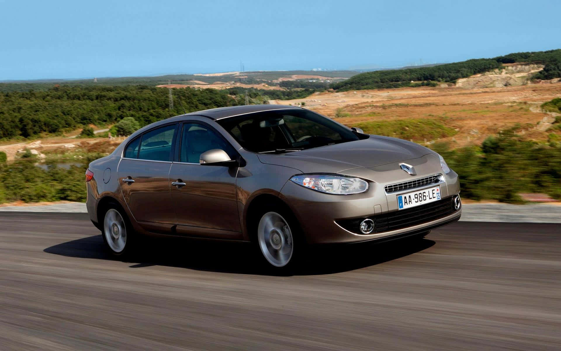 Renault Fluence 桌布 壁紙 — 一輛流線型棕色轎車沿著蜿蜒的道路疾馳，穿過陽光明媚的鄉村，背景是模糊的綠色山丘和清澈的藍天。