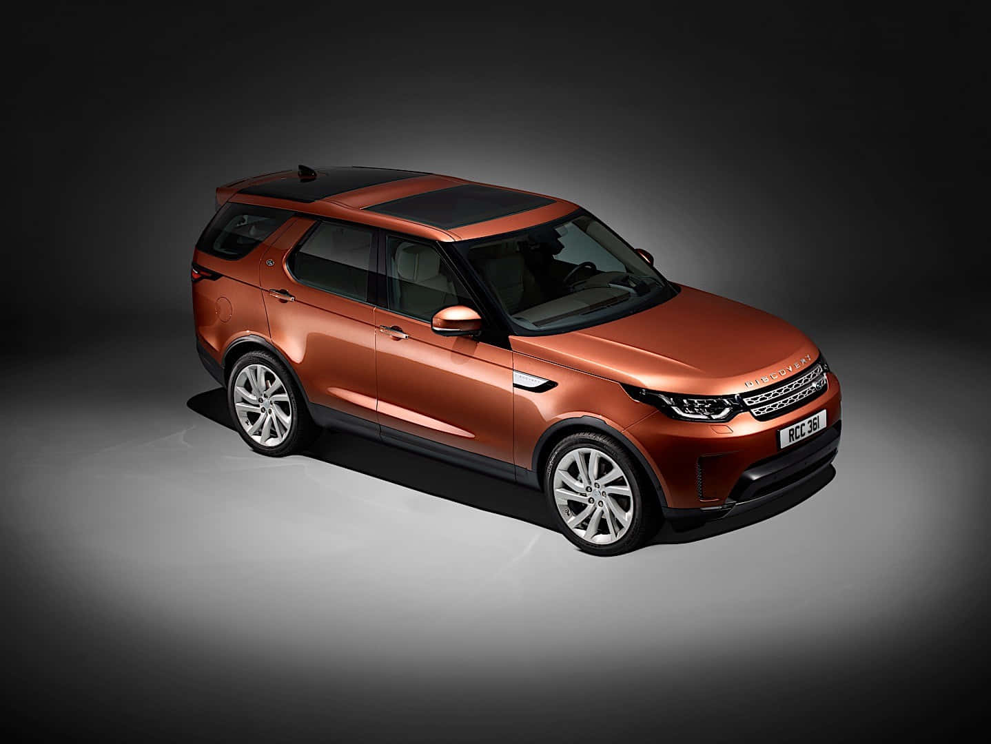 Land Rover Discovery 桌布 壁紙 — 一輛時尚的銅色Land Rover Discovery SUV在攝影棚內以戲劇性的聚光燈照射，背景為深色漸變。