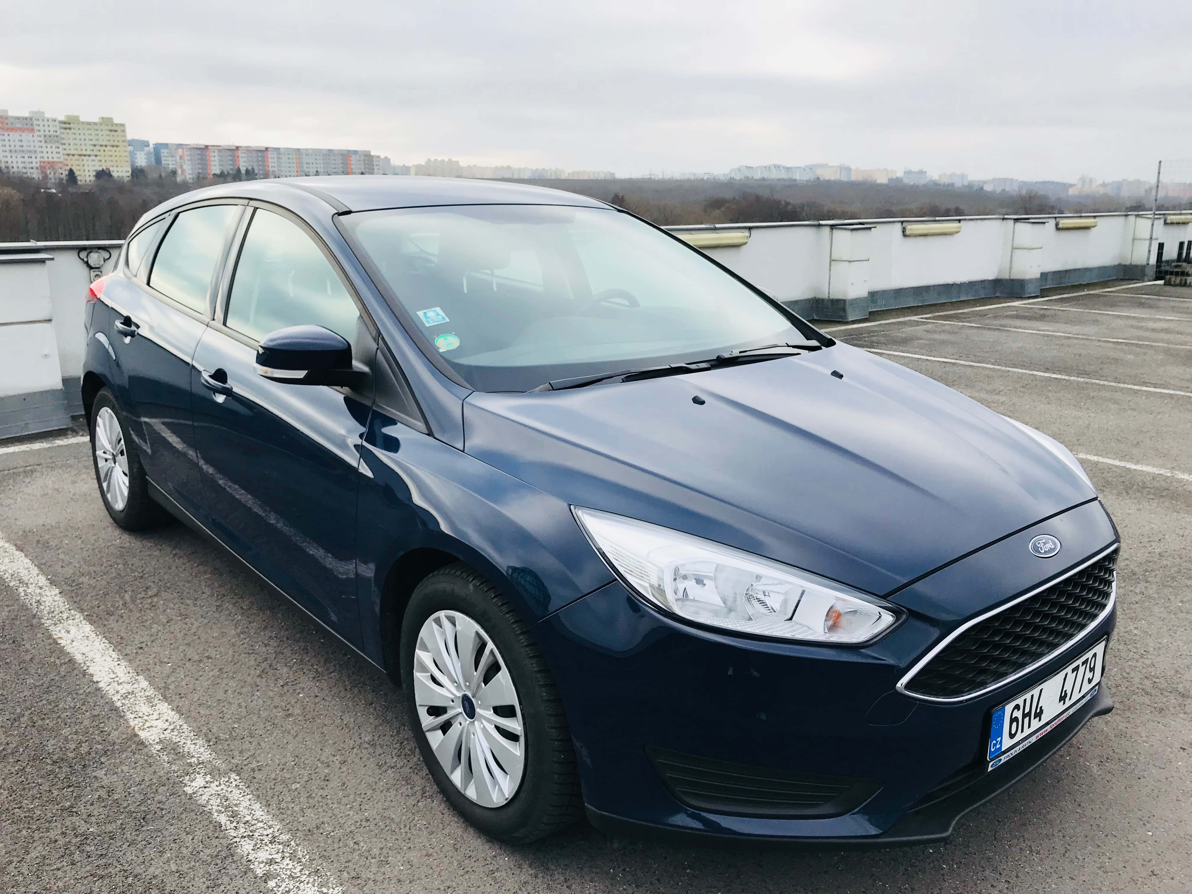 Ford Focus 桌布 壁紙 — 一架時尚的深藍色福特福克斯停泊在屋頂停車場，天空多雲，遠處有城市建築。