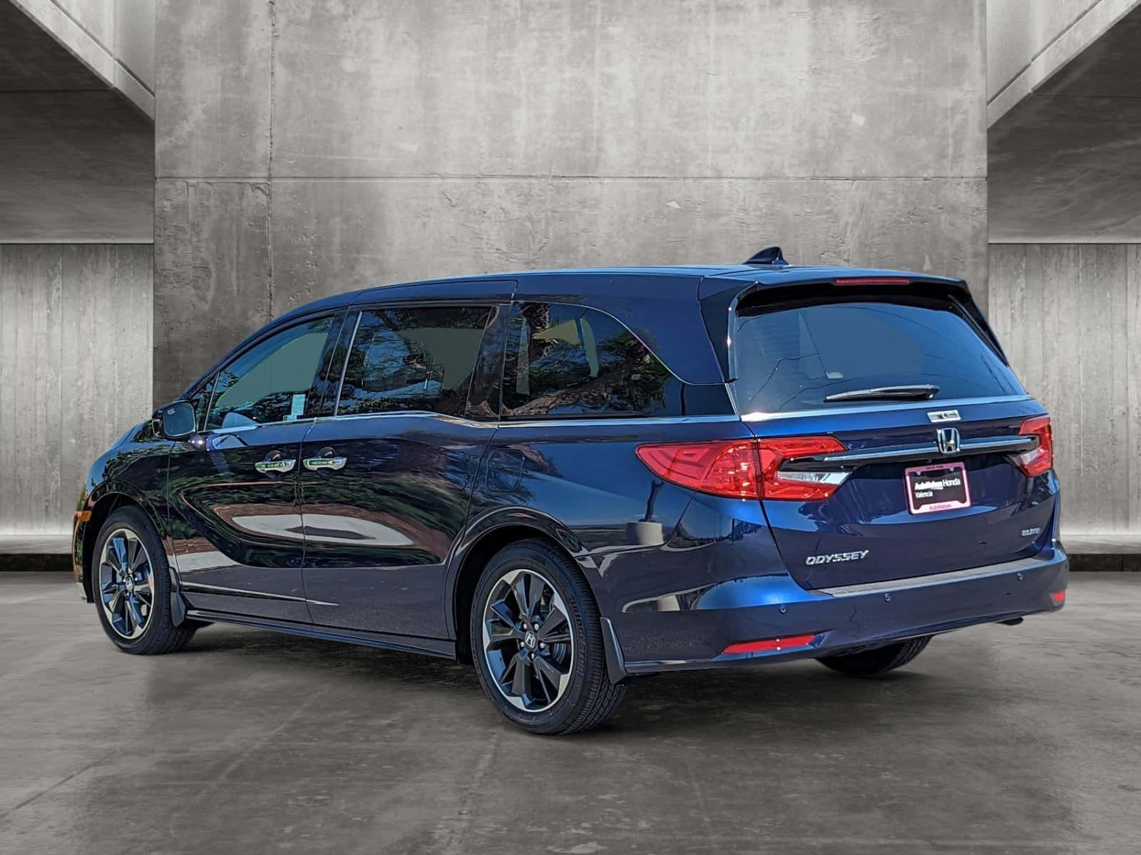 Honda Odyssey 桌布 壁紙 — 一輛時尚的深藍色本田Odyssey小型貨車在明亮的日光下停靠在有紋理的混凝土牆旁。