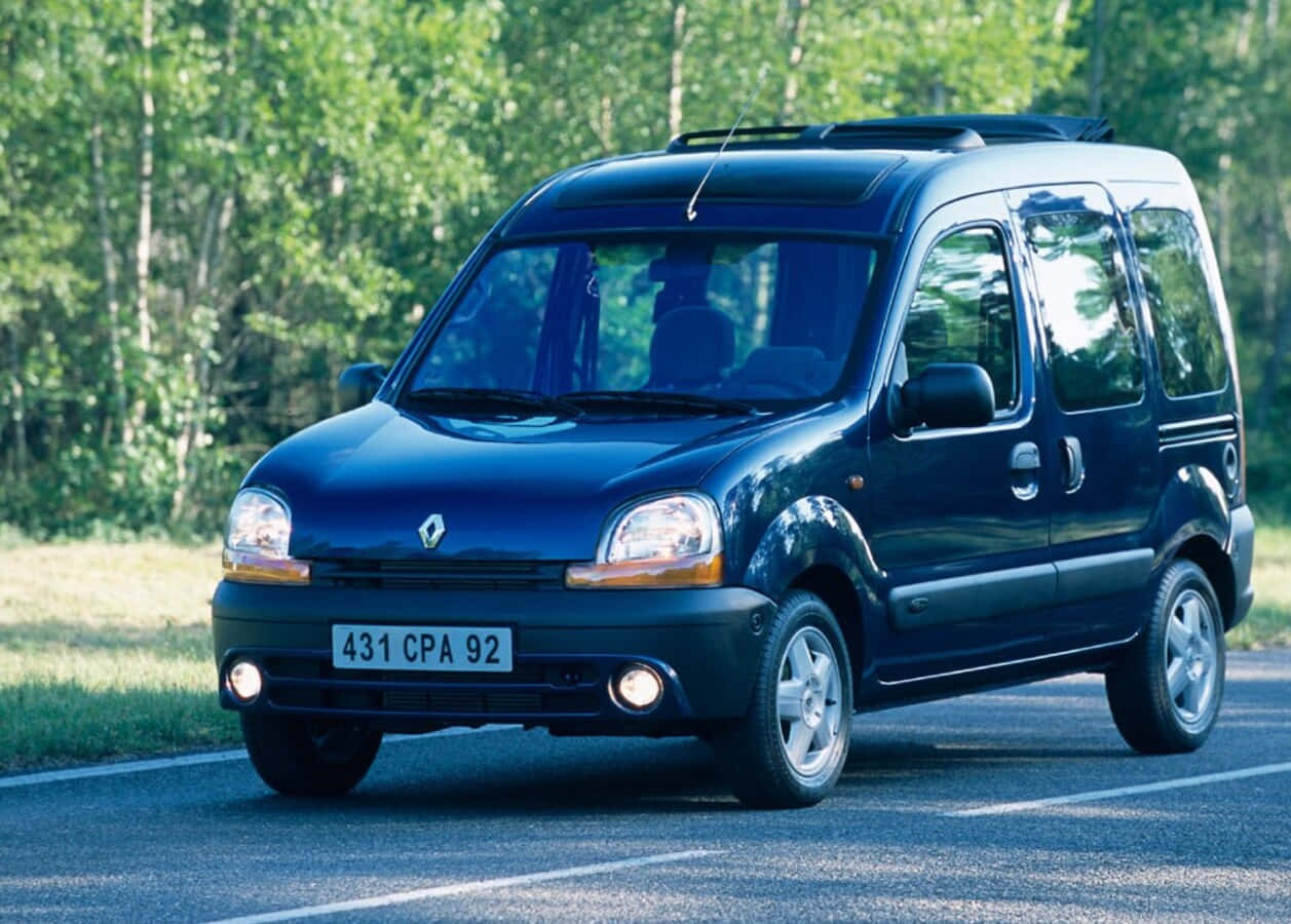 Renault Kangoo 桌布 壁紙 — 一架時尚的深藍色雷諾Kangoo客貨車在陽光明媚的森林道路上行駛，背景是綠樹。