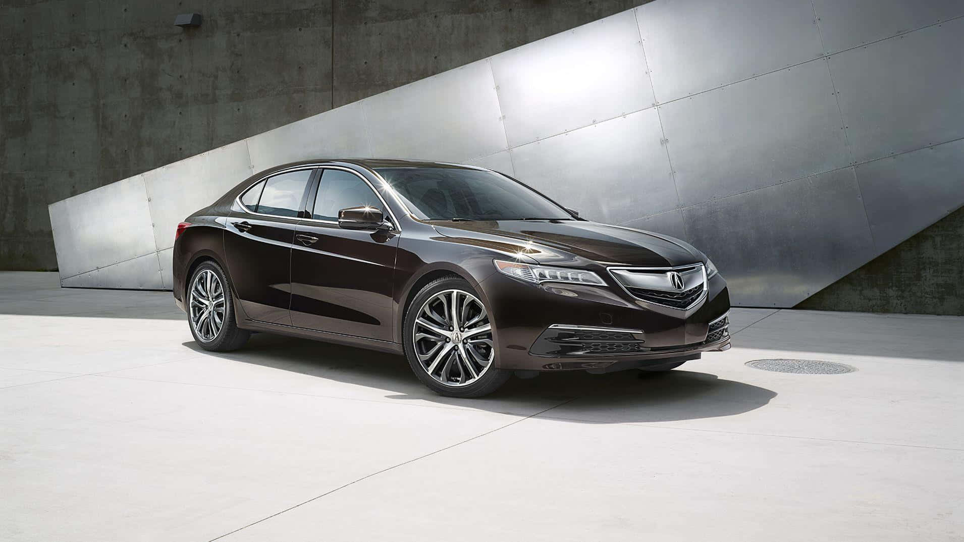 Acura Tlx 桌布 壁紙 — 一輛時尚的深棕色豪華轎車在明亮的日光下停靠在現代混凝土和金屬牆旁。