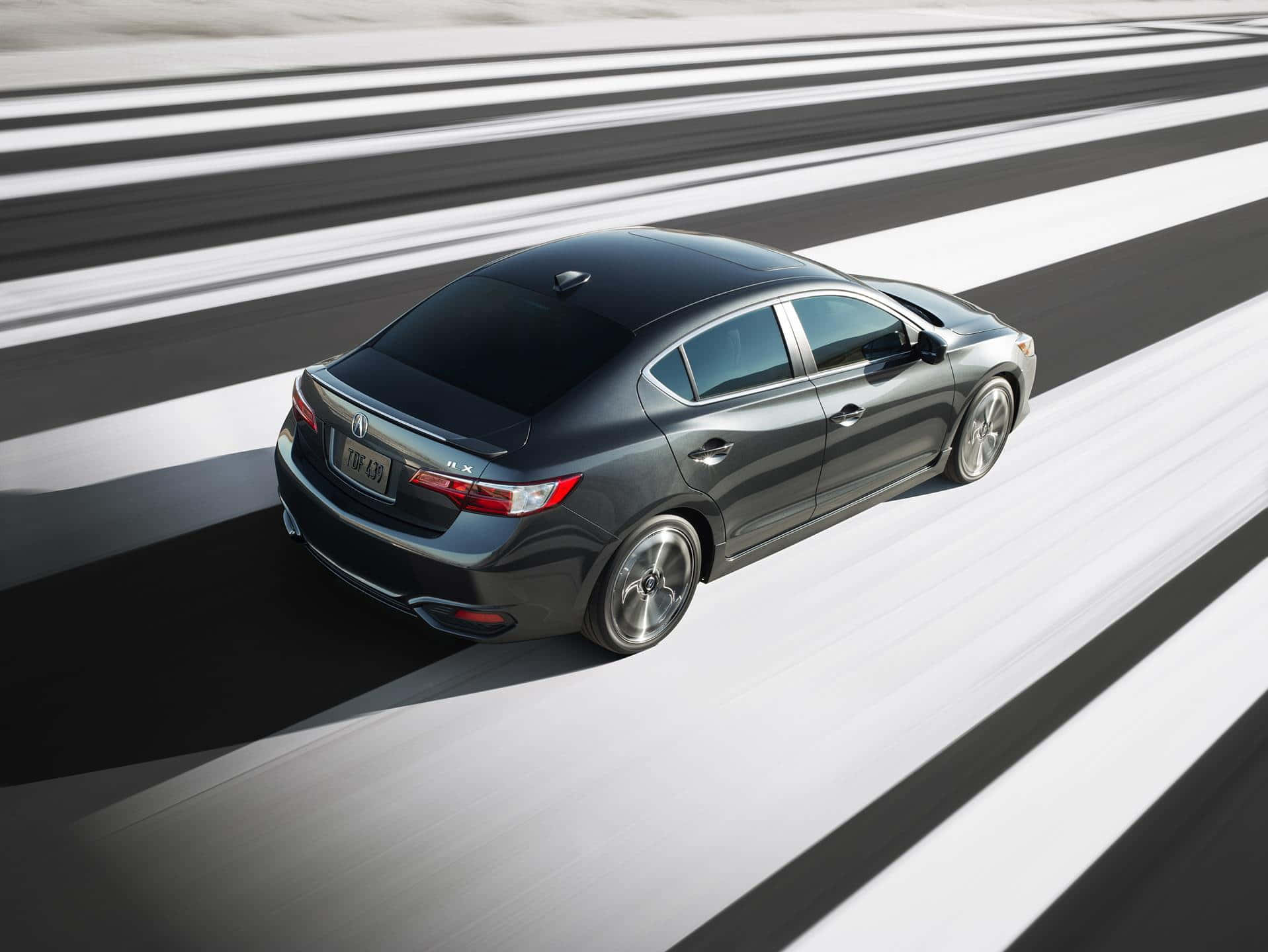 Acura Ilx 桌布 壁紙 — 一輛時尚的深灰色轎車在模糊的高速公路上疾馳，大膽的黑白條紋營造出動態的運動效果。
