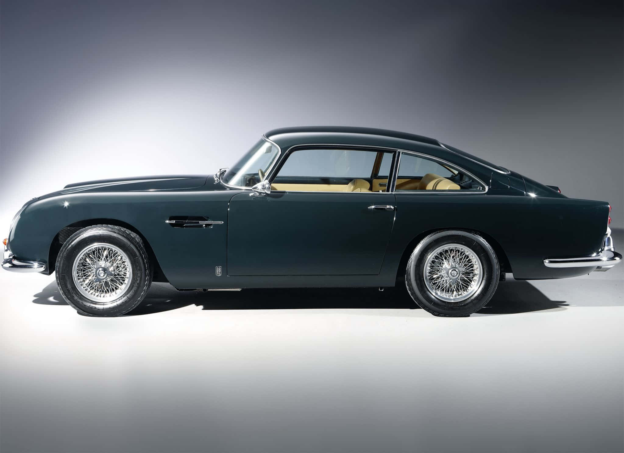 Aston Martin Db5 桌布 壁紙 — 一輛時尚的深綠色經典 Aston Martin DB5 在漸變灰色工作室背景前展示側面，可見米色內飾。