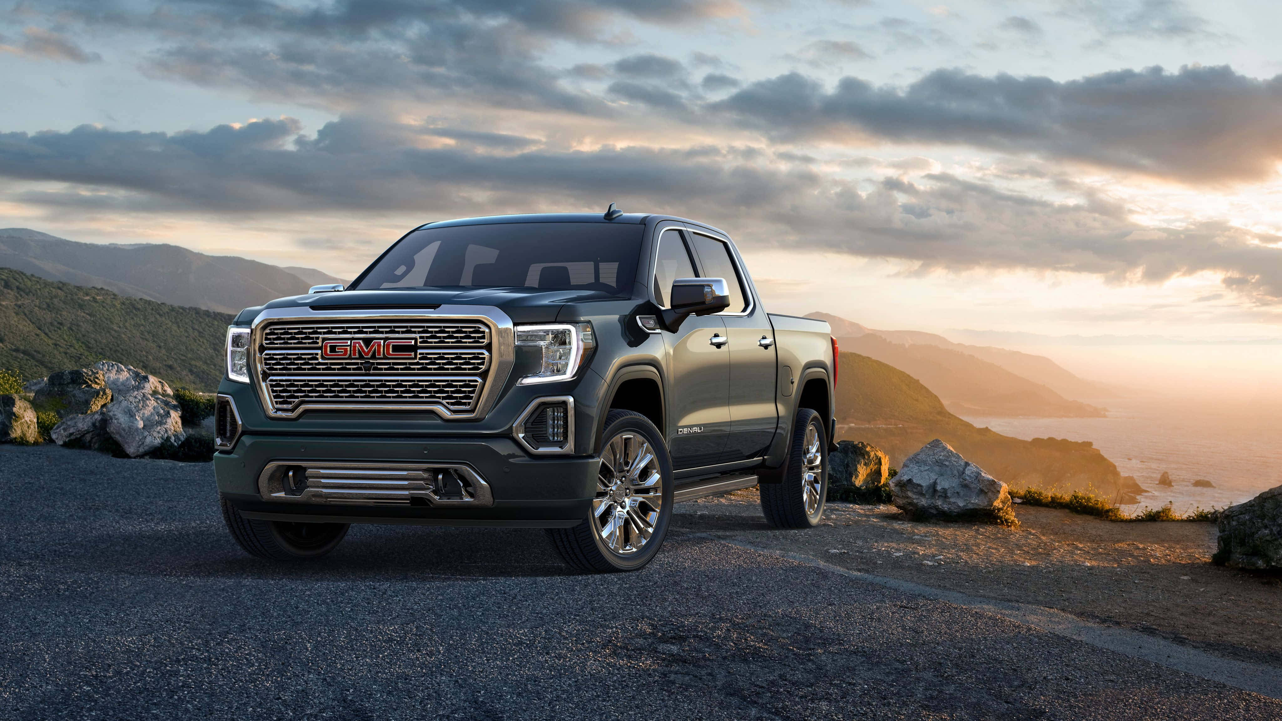 Gmc Yukon 桌布 壁紙 — 一架時尚的深綠色 GMC Sierra 皮卡車停在日落時分的海岸懸崖上，背景有山脈和海洋。