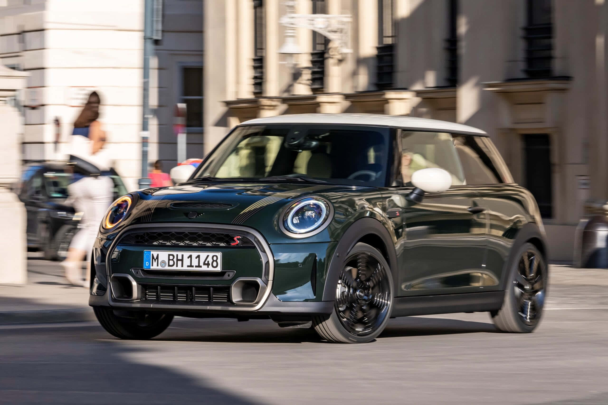 Mini Cooper S 桌布 壁紙 — 一輛時尚的深綠色MINI Cooper S配白色車頂，行駛在陽光明媚的歐洲城市街道上。