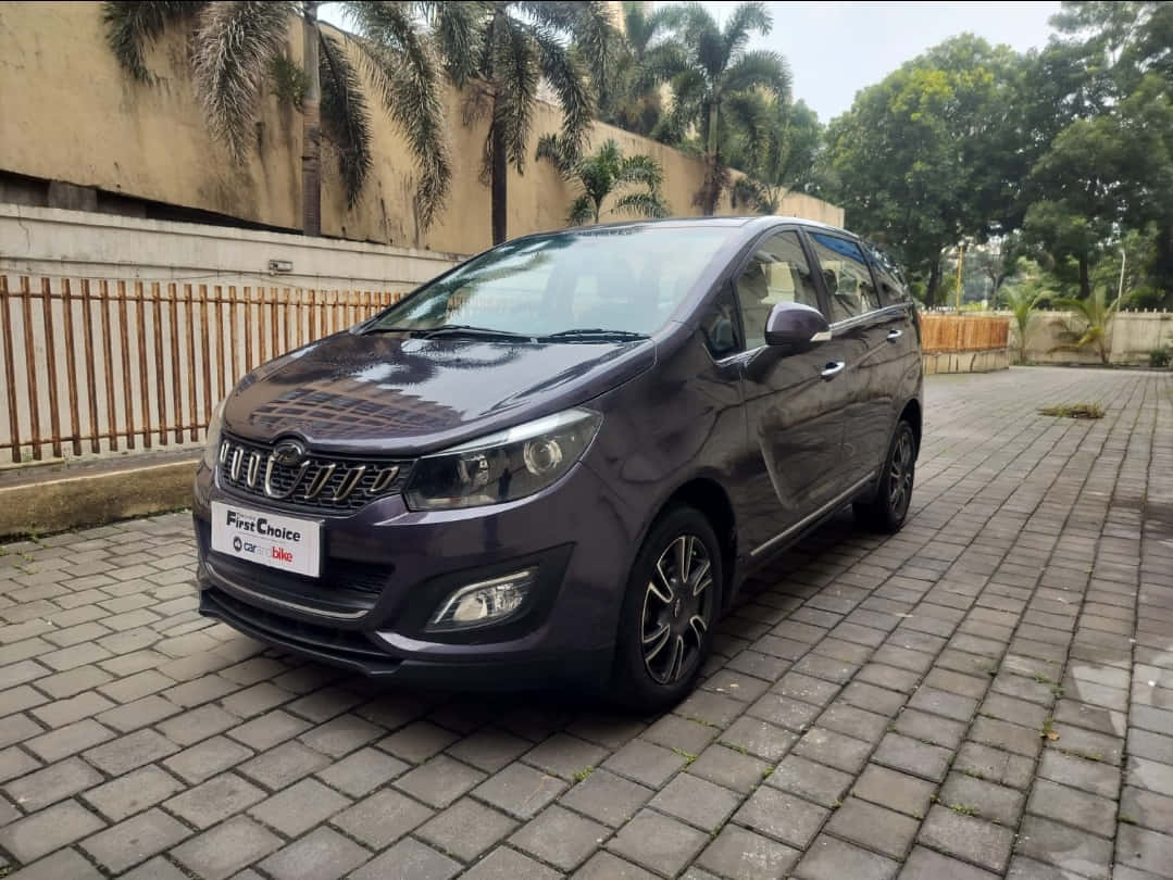 Mahindra Marazzo 桌布 壁紙 — 一架時尚的深紫色緊湊型MPV停泊在灰色磚砌車道上，背景有棕櫚樹和米色牆壁。