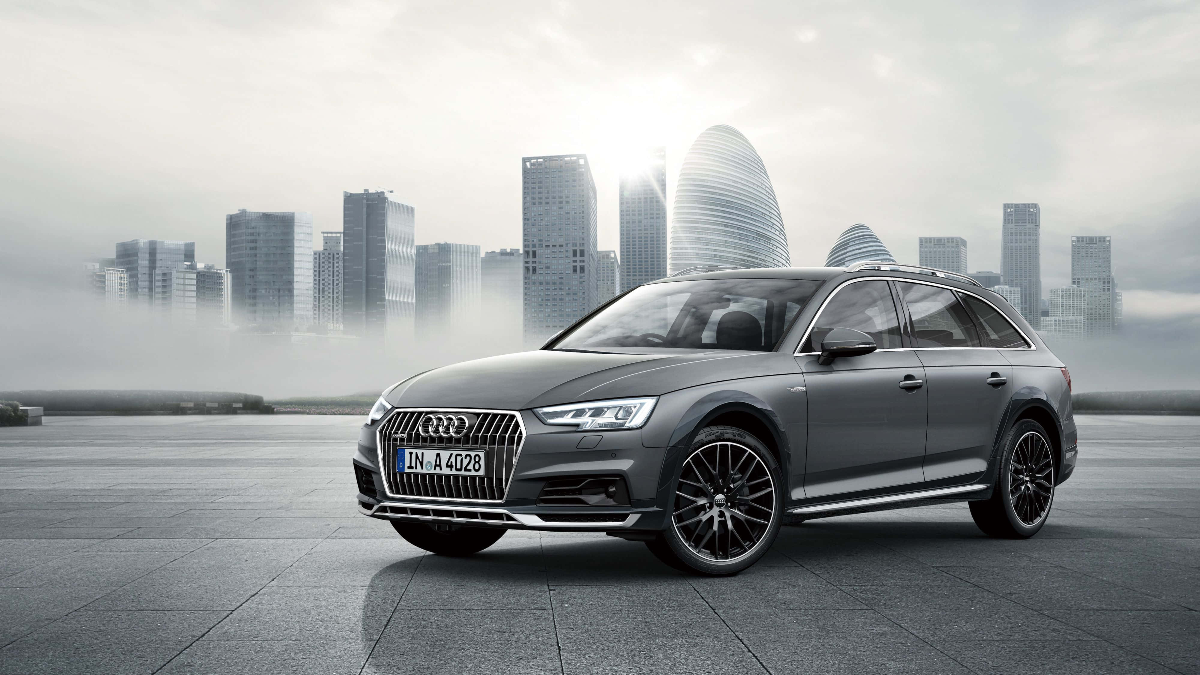 Audi A4 桌布 壁紙 — 一架時尚的灰色奧迪旅行車停泊在霧氣瀰漫的都市廣場上，現代摩天大樓在柔和的晨光中閃耀。
