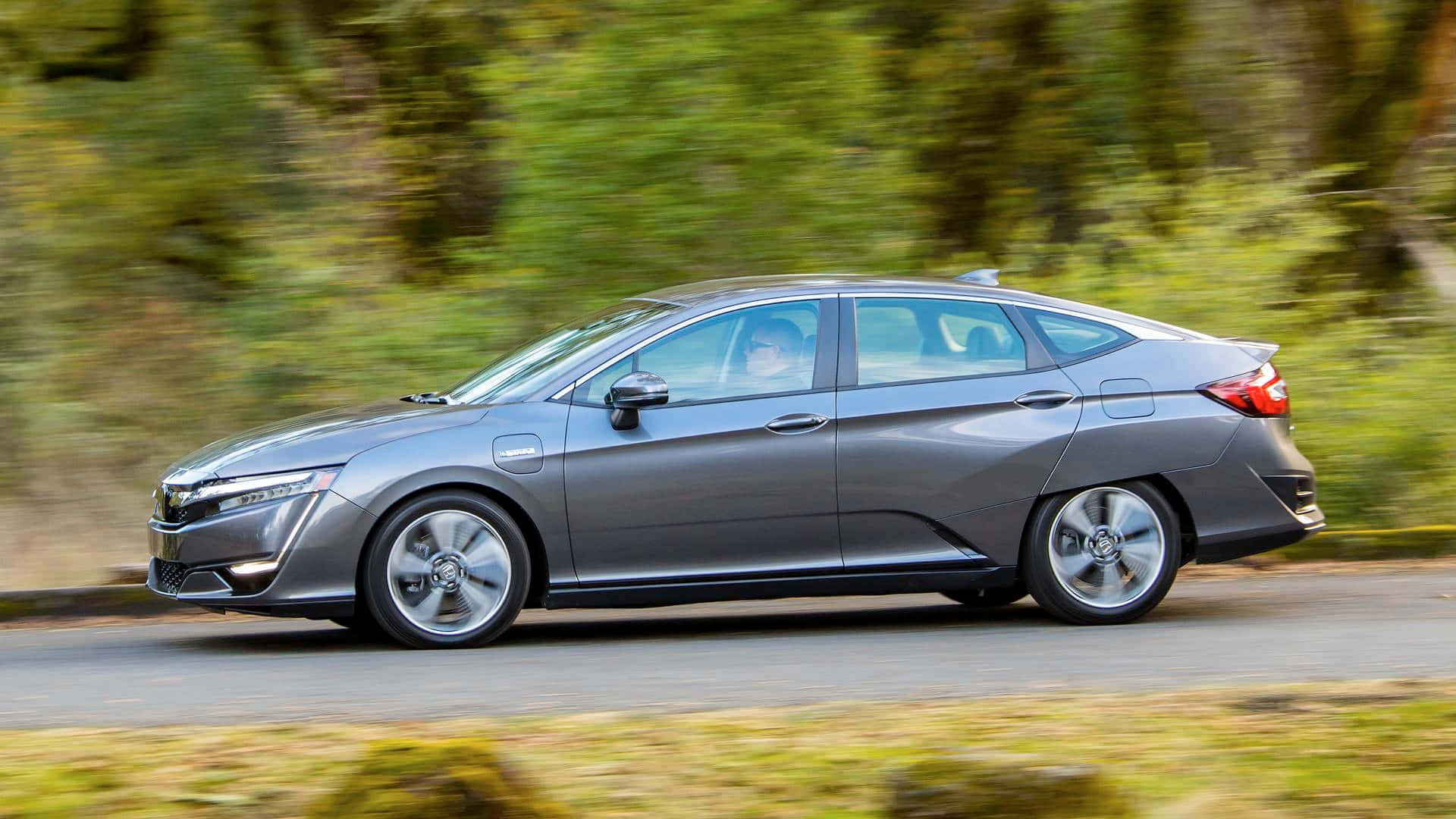 Honda Clarity 桌布 壁紙 — 一輛時尚的灰色電動車在森林環繞的道路上行駛，背景帶有動態模糊效果。