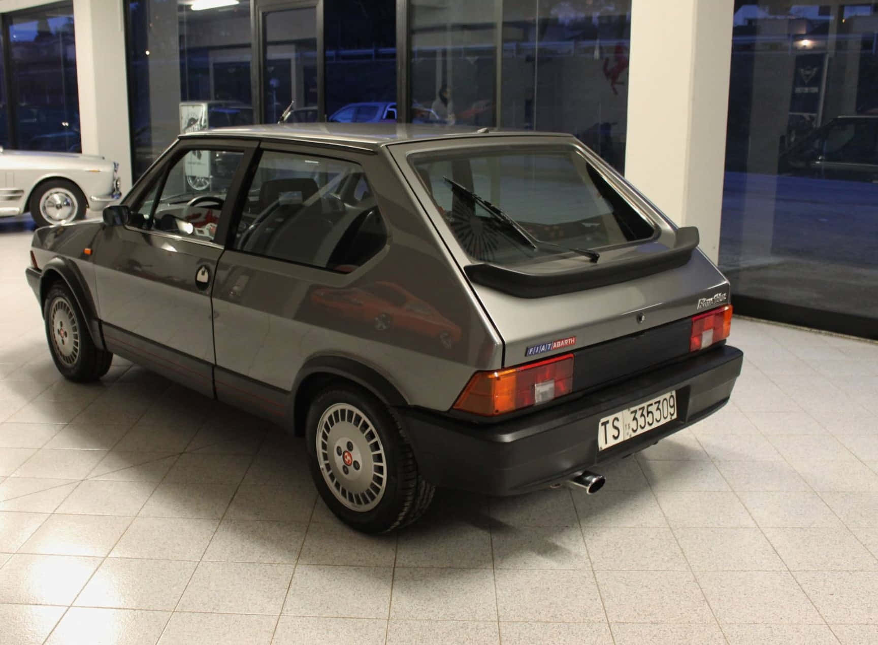 Fiat Ritmo 桌布 壁紙 — 一架時尚的灰色菲亞特 Panda 4x4 在室內瓷磚地板上展示，玻璃牆上有倒影。