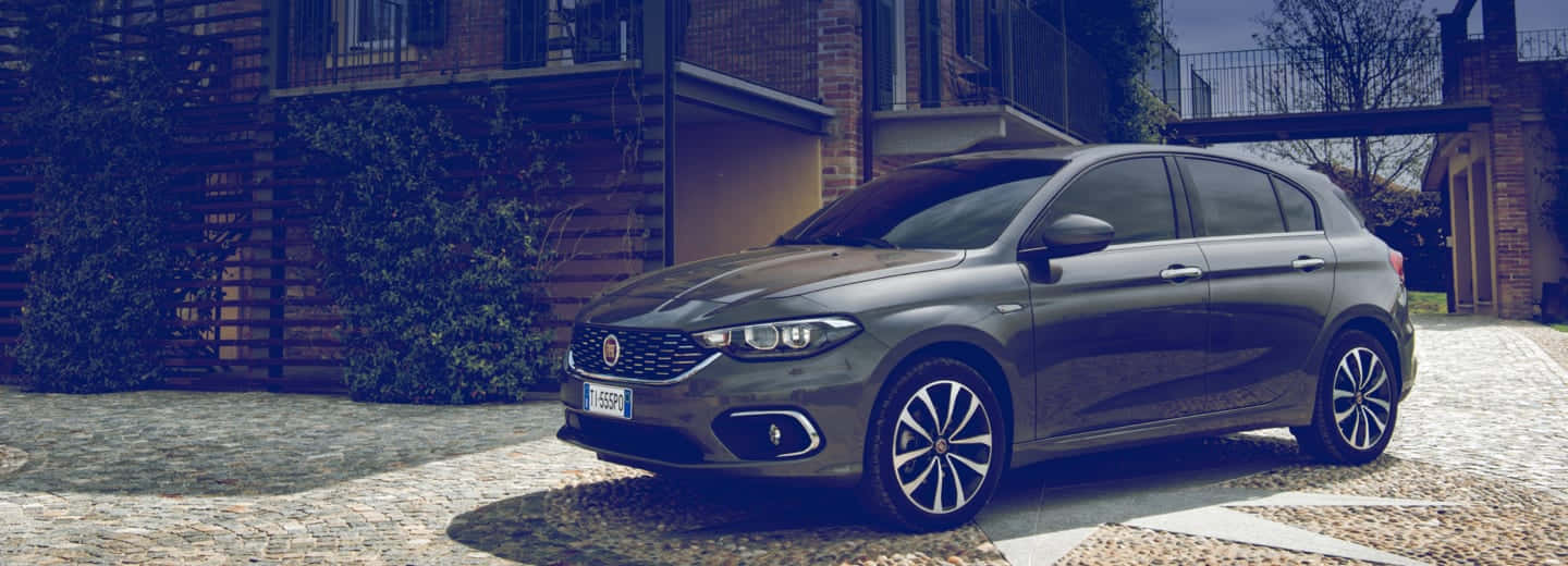 Fiat Tipo 桌布 壁紙 — 一架時尚的灰色 Fiat Punto 停泊在鵝卵石車道上，旁邊是一棟現代磚砌房屋，牆上爬滿了常春藤。