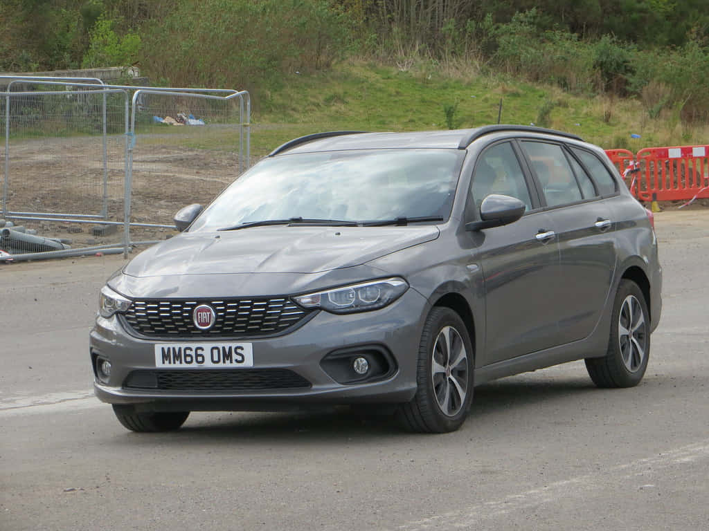 Fiat Tipo 桌布 壁紙 — 一架時尚的灰色Fiat旅行車停在瀝青路上，背景有綠化和建築圍欄。