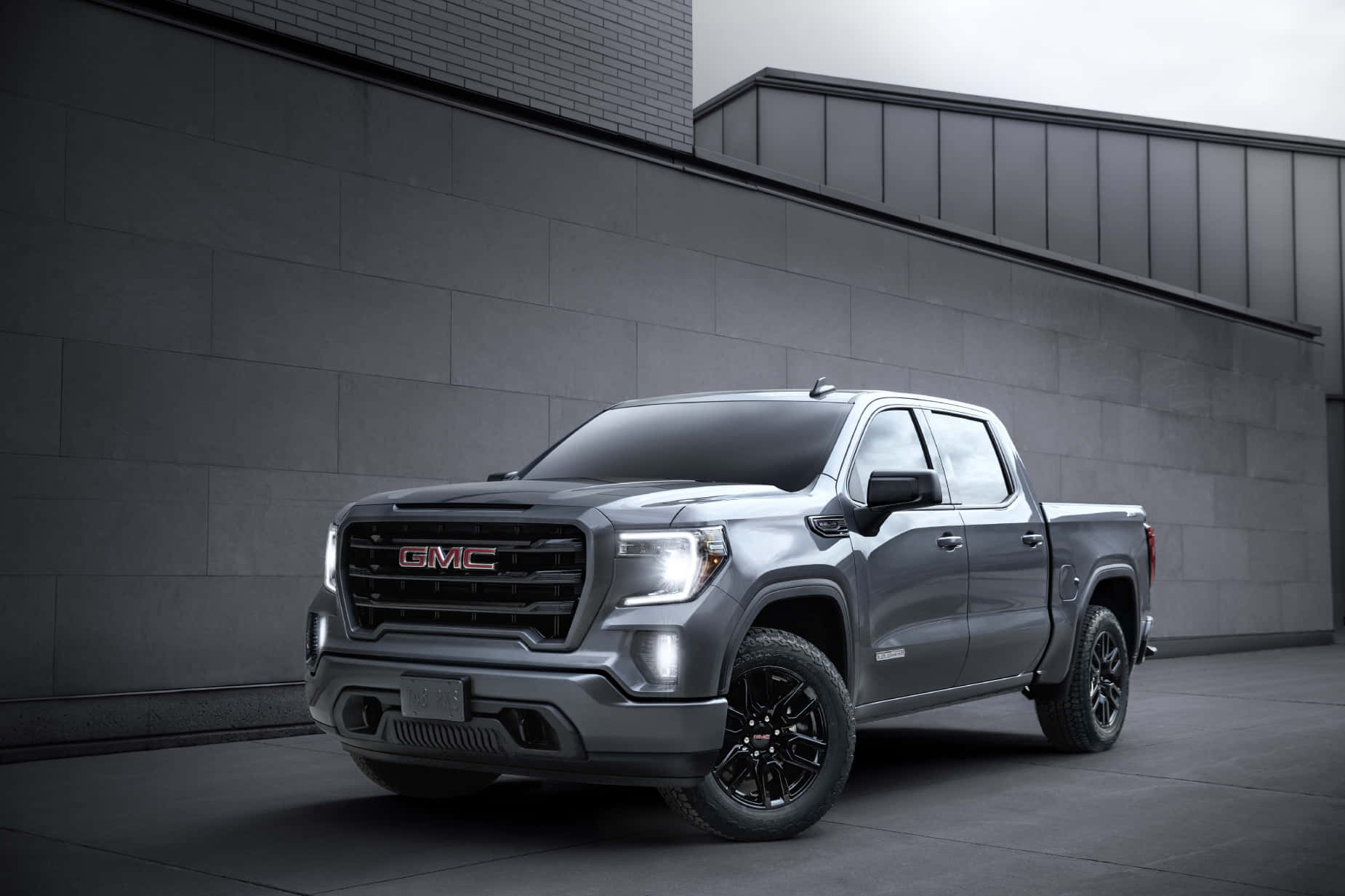 Gmc Sierra 桌布 壁紙 — 一架時尚的灰色GMC Sierra皮卡車，配備黑色輪圈，停放在現代灰色混凝土牆前，天空多雲。