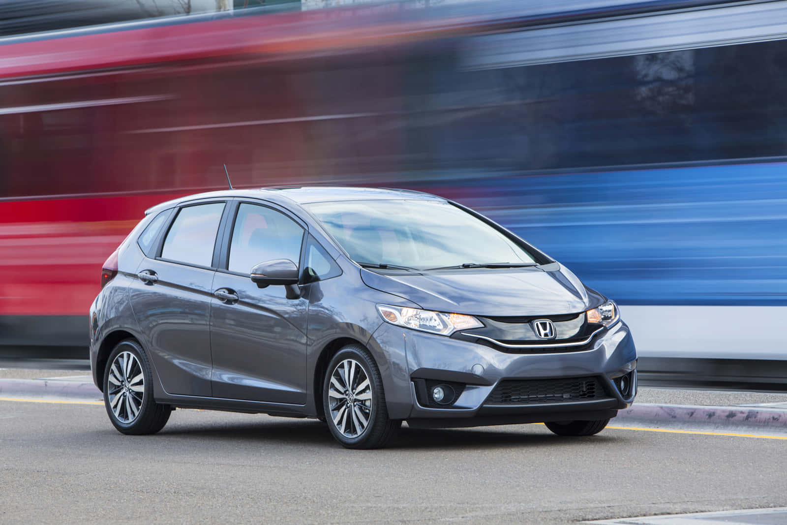 Honda Fit 桌布 壁紙 — 一輛時尚的灰色本田飛度在城市的街道上飛馳，身後留下模糊的紅色和藍色運動條紋。